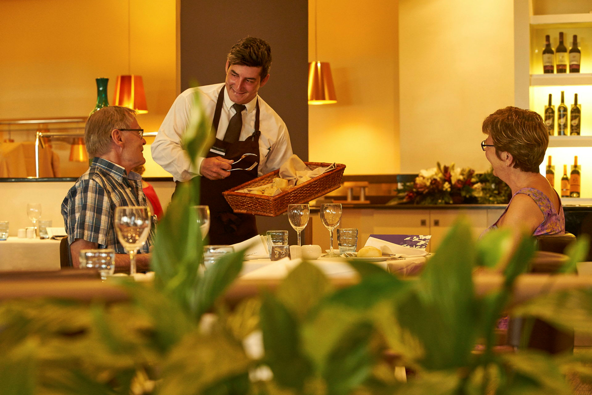 En servitør tilbyr brød til gjester ved et dekket bord på en restaurant. (AI-generert tekst)