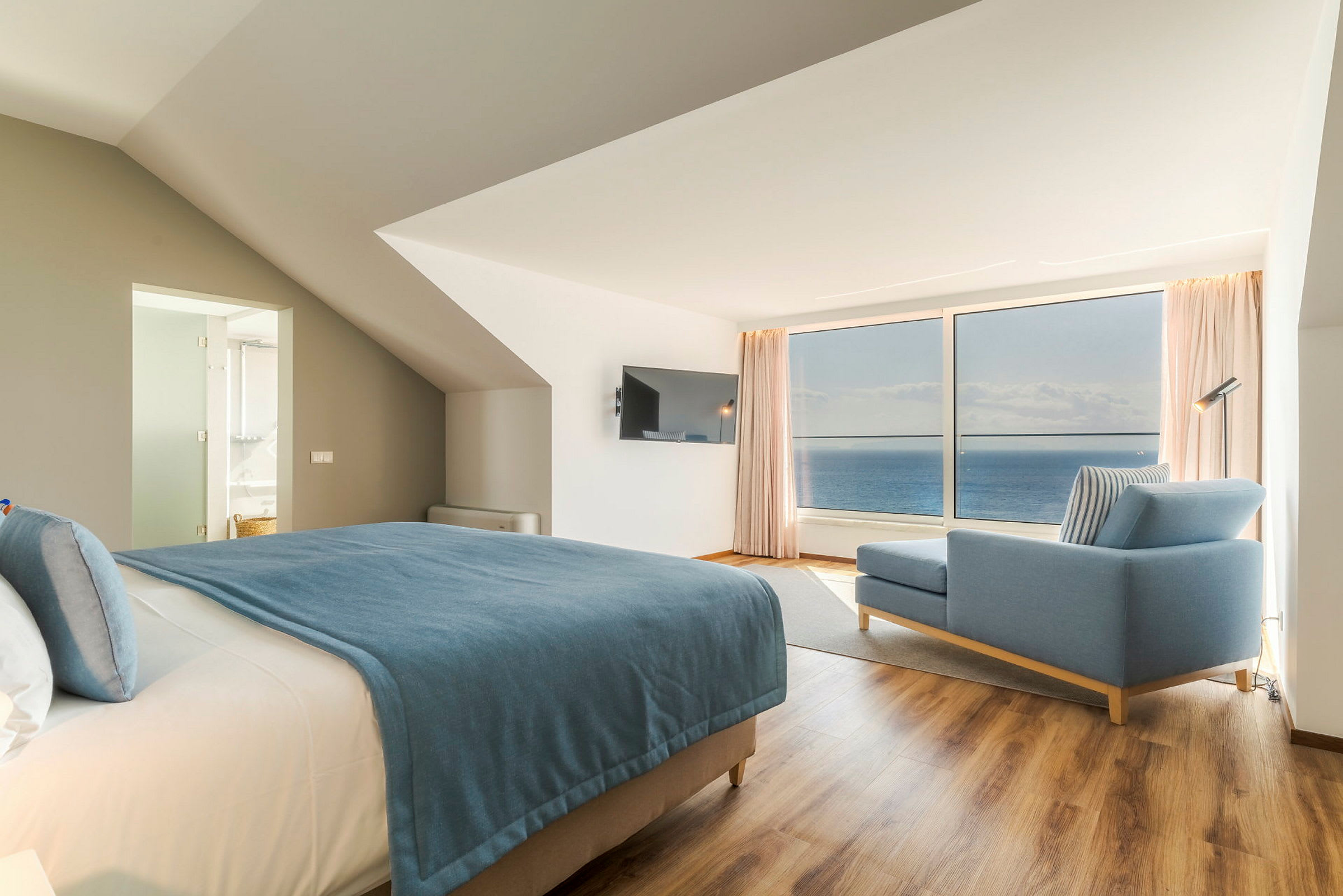 Moderne hotellrom med havutsikt, seng med blått sengeteppe og blå sofa. (AI-generert tekst)