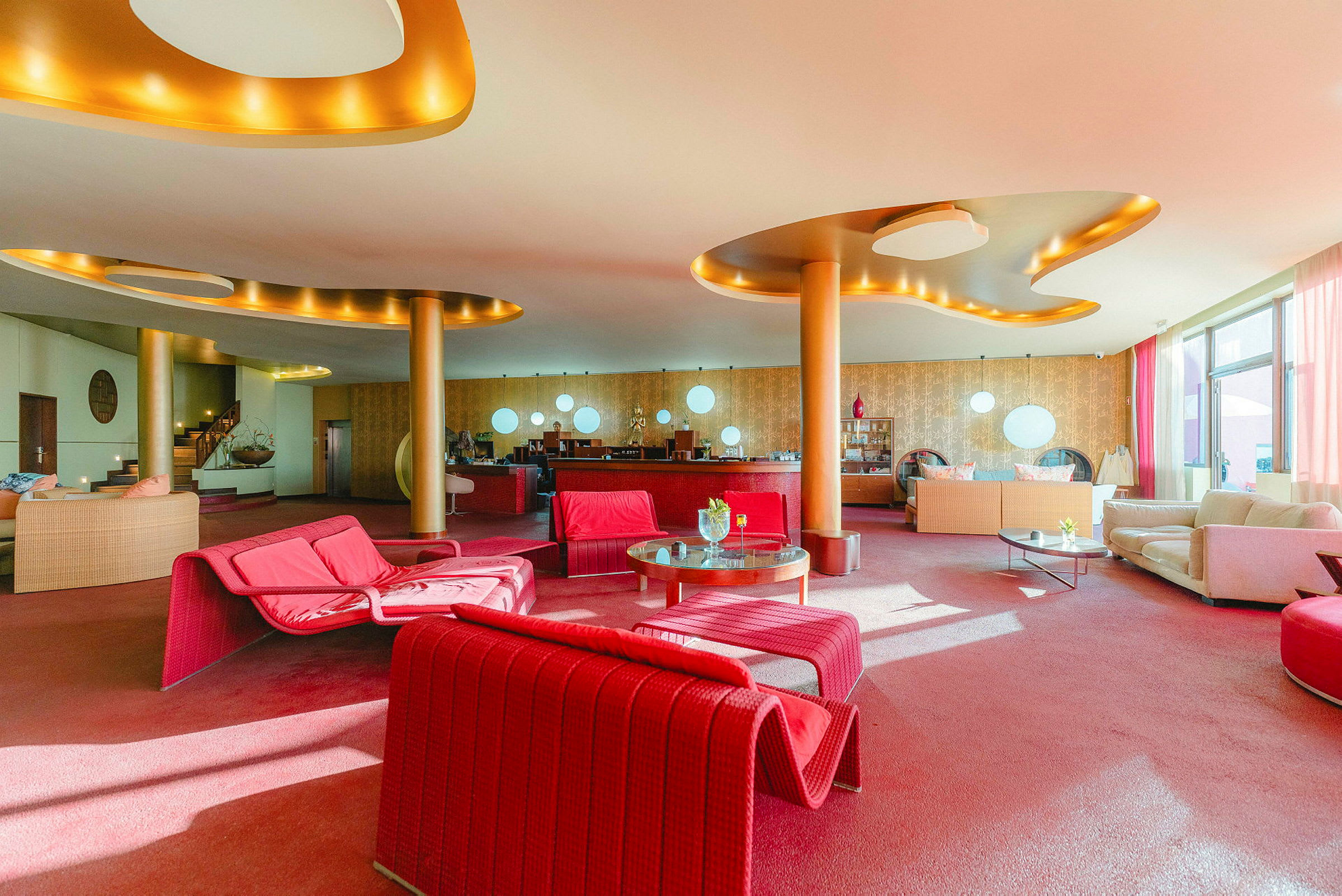 En hotellobby med fargerike møbler, hovedsakelig røde og beige. Det er sofaer, bord og moderne interiørdetaljer. (AI-generert tekst)