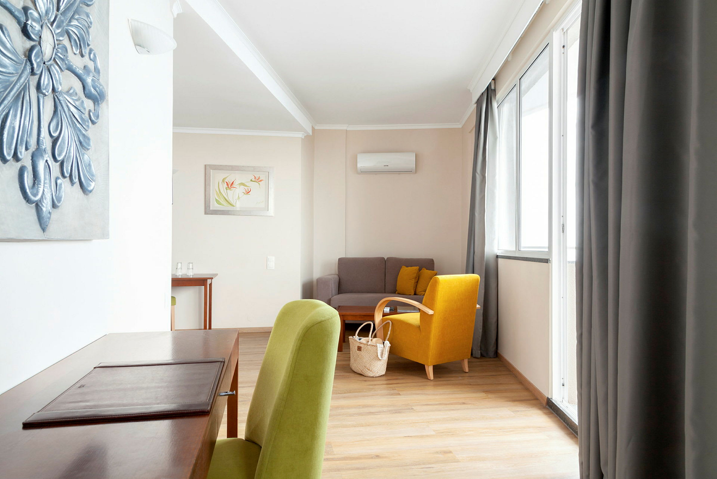 Et velmøblert stue med en grønn og en gul stol, en sofa og et skrivebord. (AI-generert tekst)