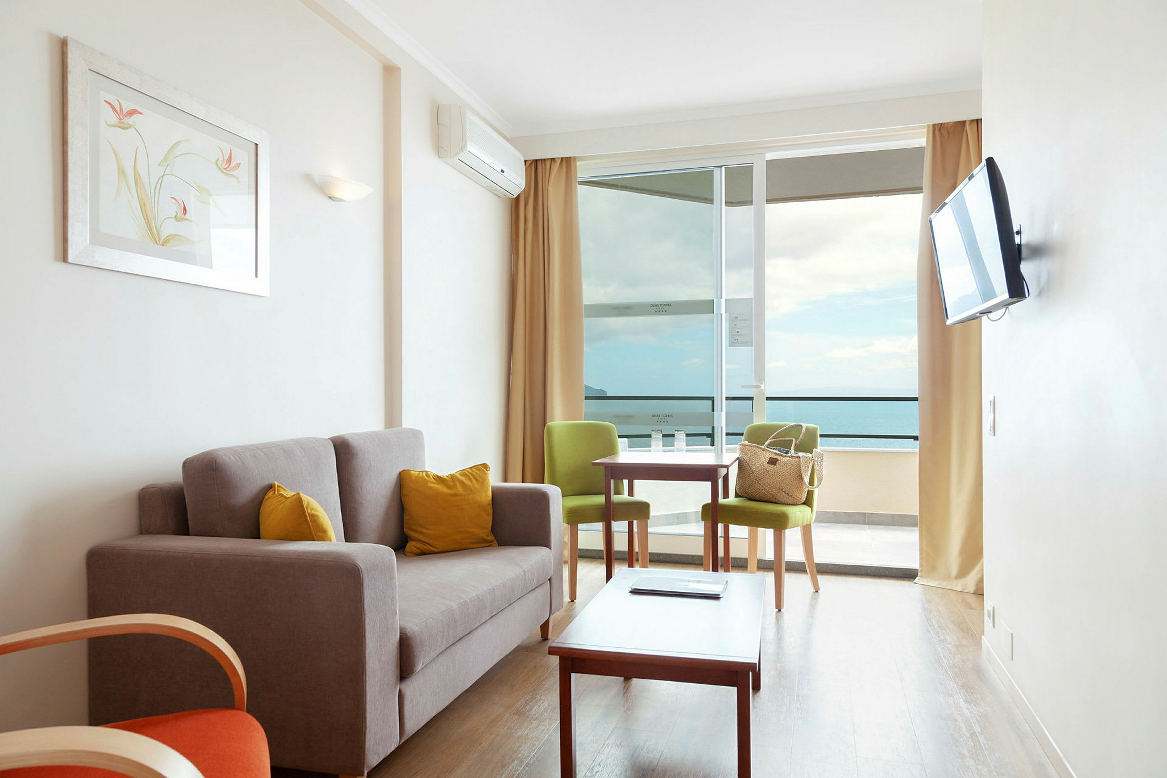 En stue med sofa, to stoler, et bord og en stor balkong med utsikt over havet. (AI-generert tekst)