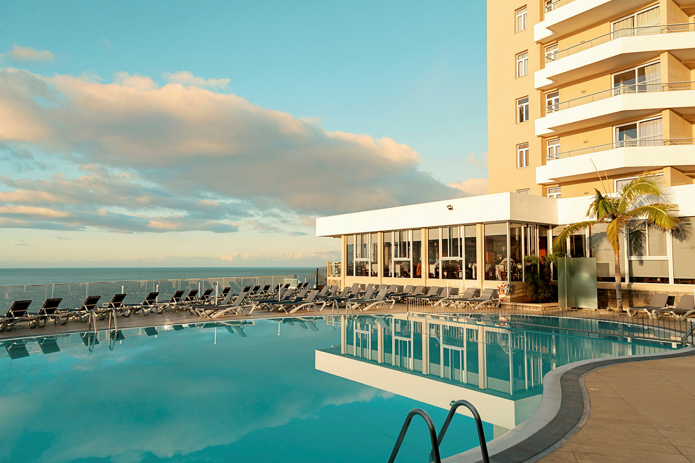 Utendørsbasseng ved hotell med solsenger og havutsikt. (AI-generert tekst)