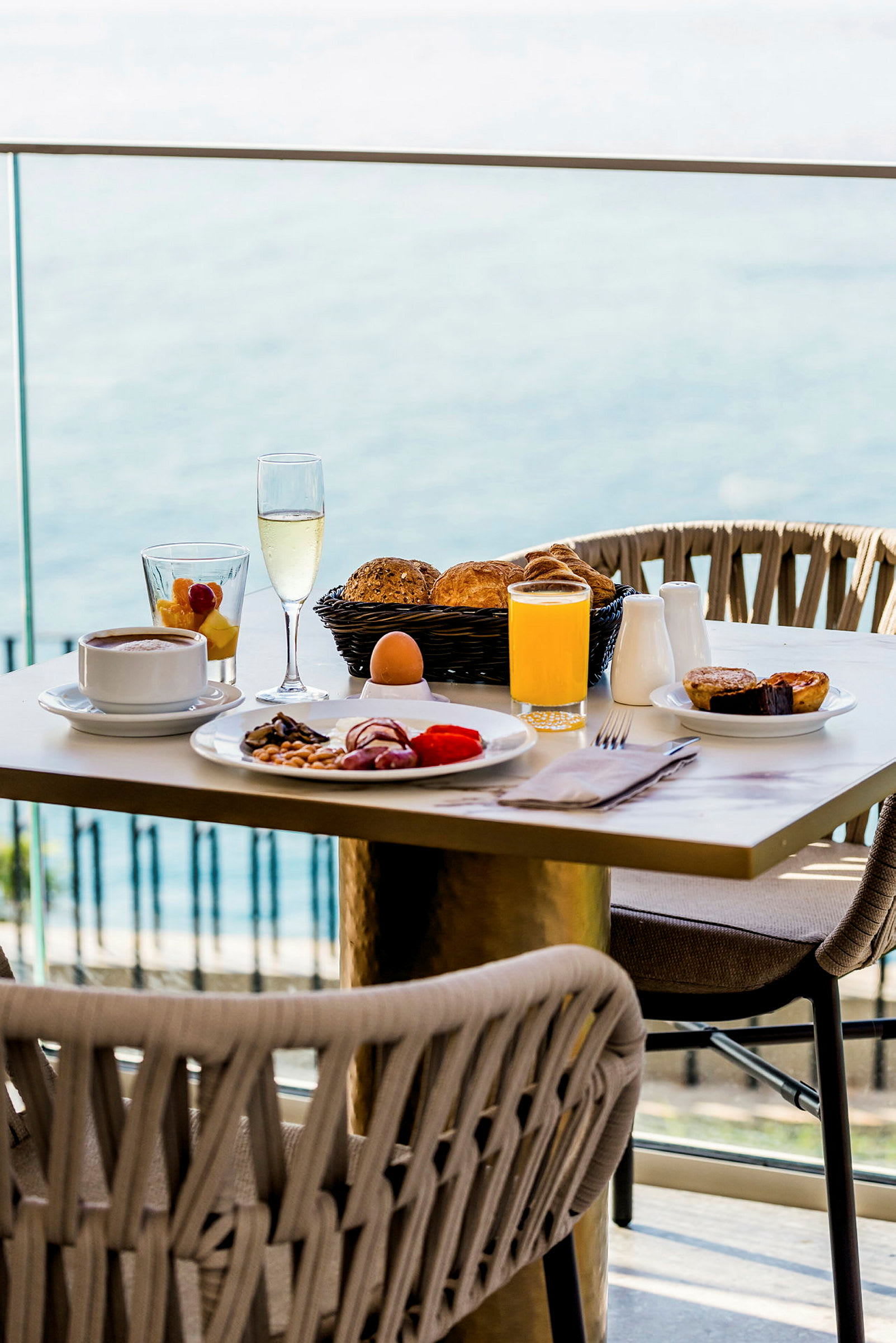 Frokostbord med forskjellige retter, drikke og brød, med havutsikt i bakgrunnen. (AI-generert tekst)