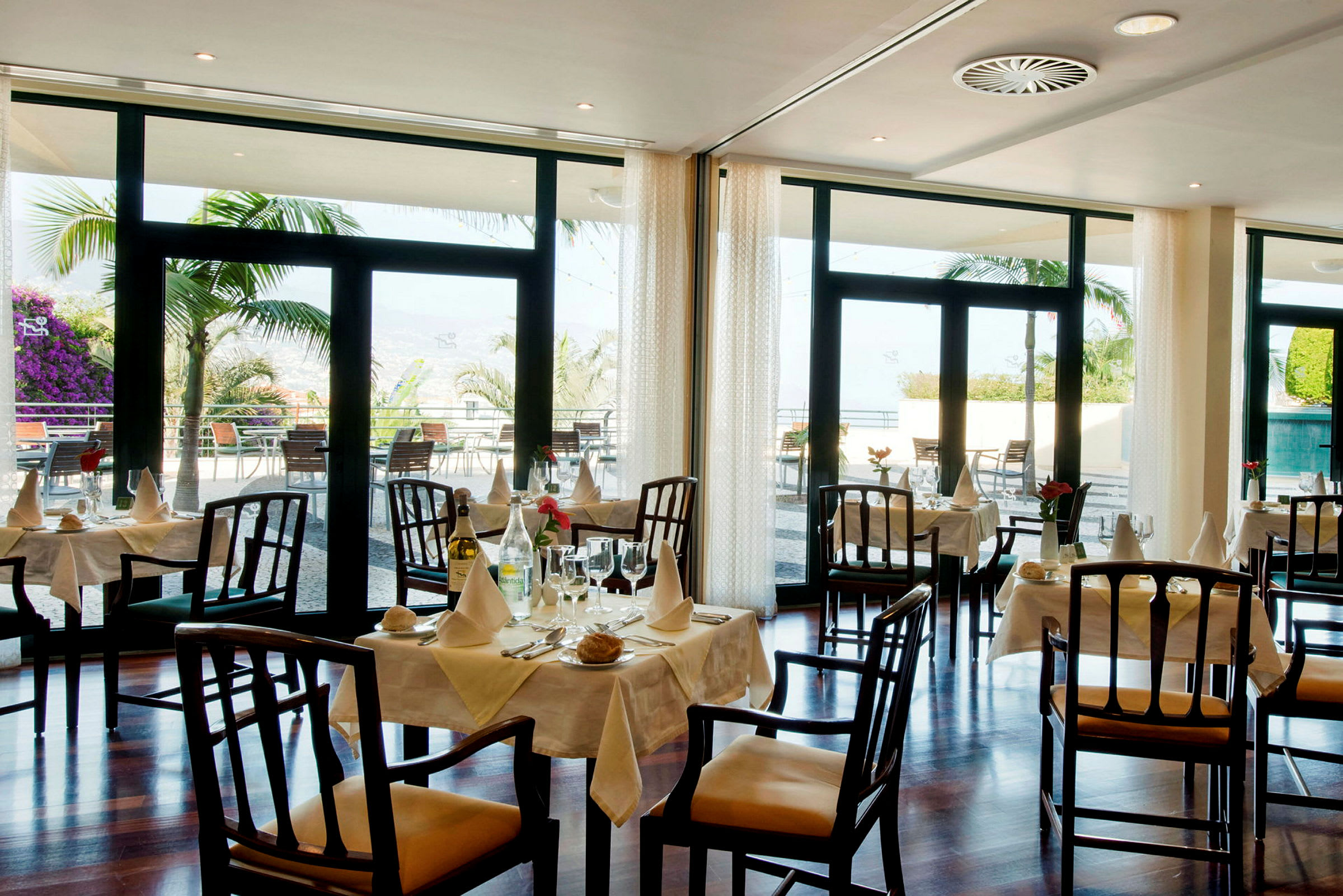 En hyggelig restaurant med dekkede bord og utsikt mot en veranda med palmetrær. (AI-generert tekst)
