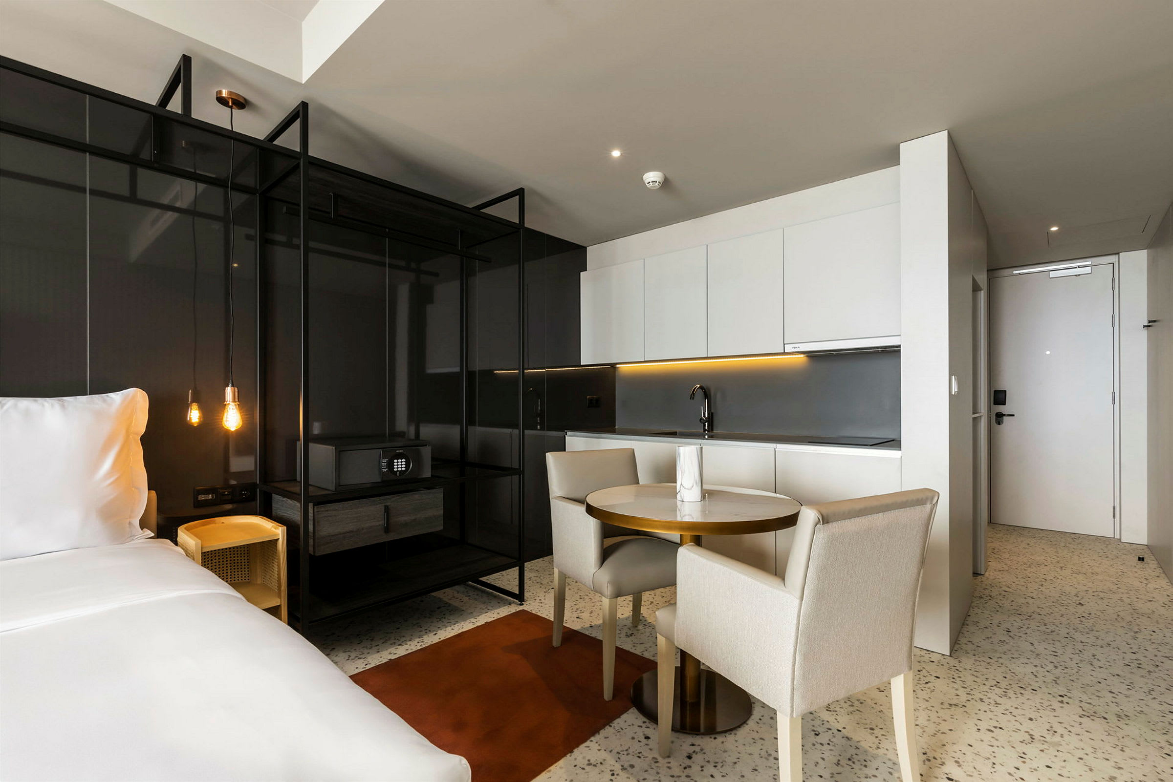 Et moderne hotellrom med åpen planløsning som inkluderer en dobbeltseng, kjøkken og spisebord. (AI-generert tekst)