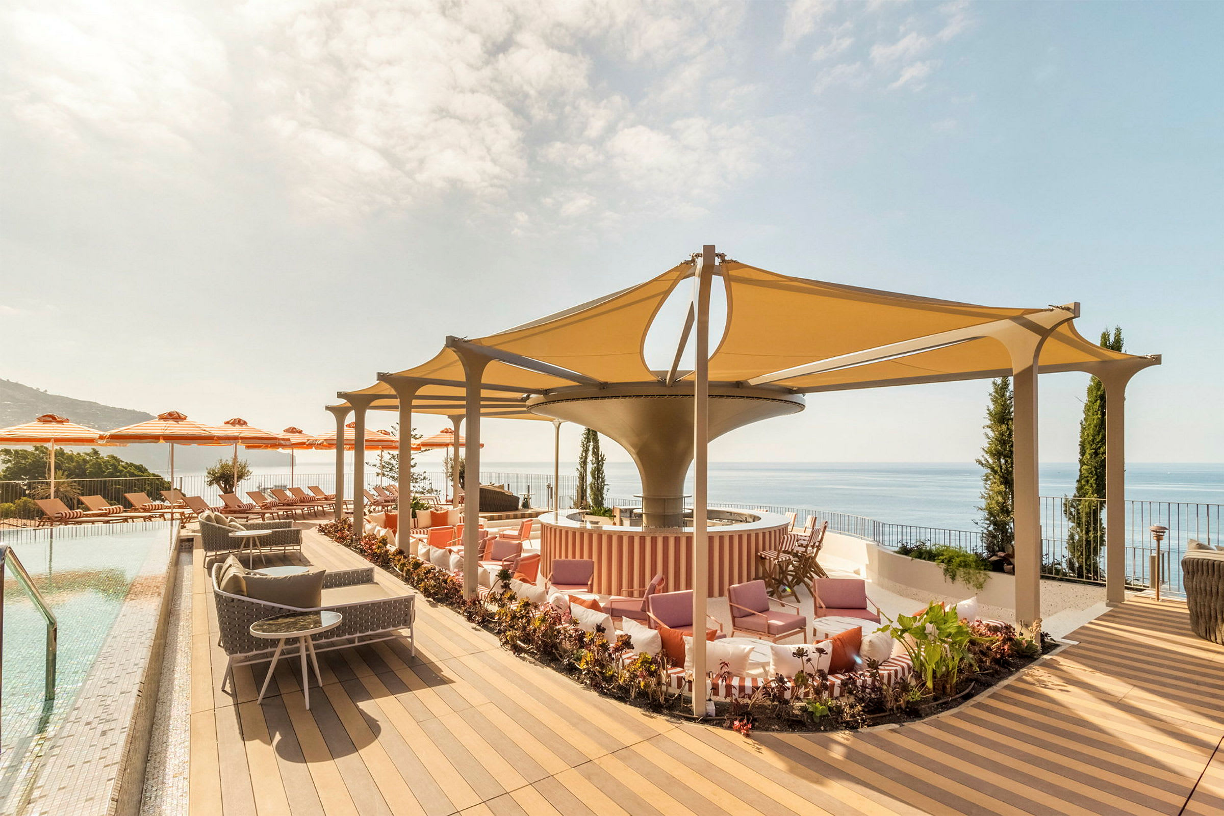 En terrasse med basseng, solsenger, parasoller og sitteplasser under et skyggefullt tak. Utsikt mot havet. (AI-generert tekst)