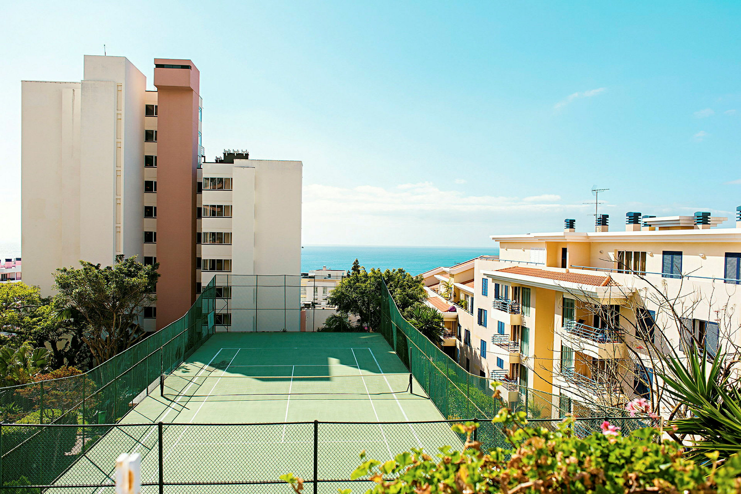 Utsikt over tennisbane med høye bygninger og havet i bakgrunnen. (AI-generert tekst)