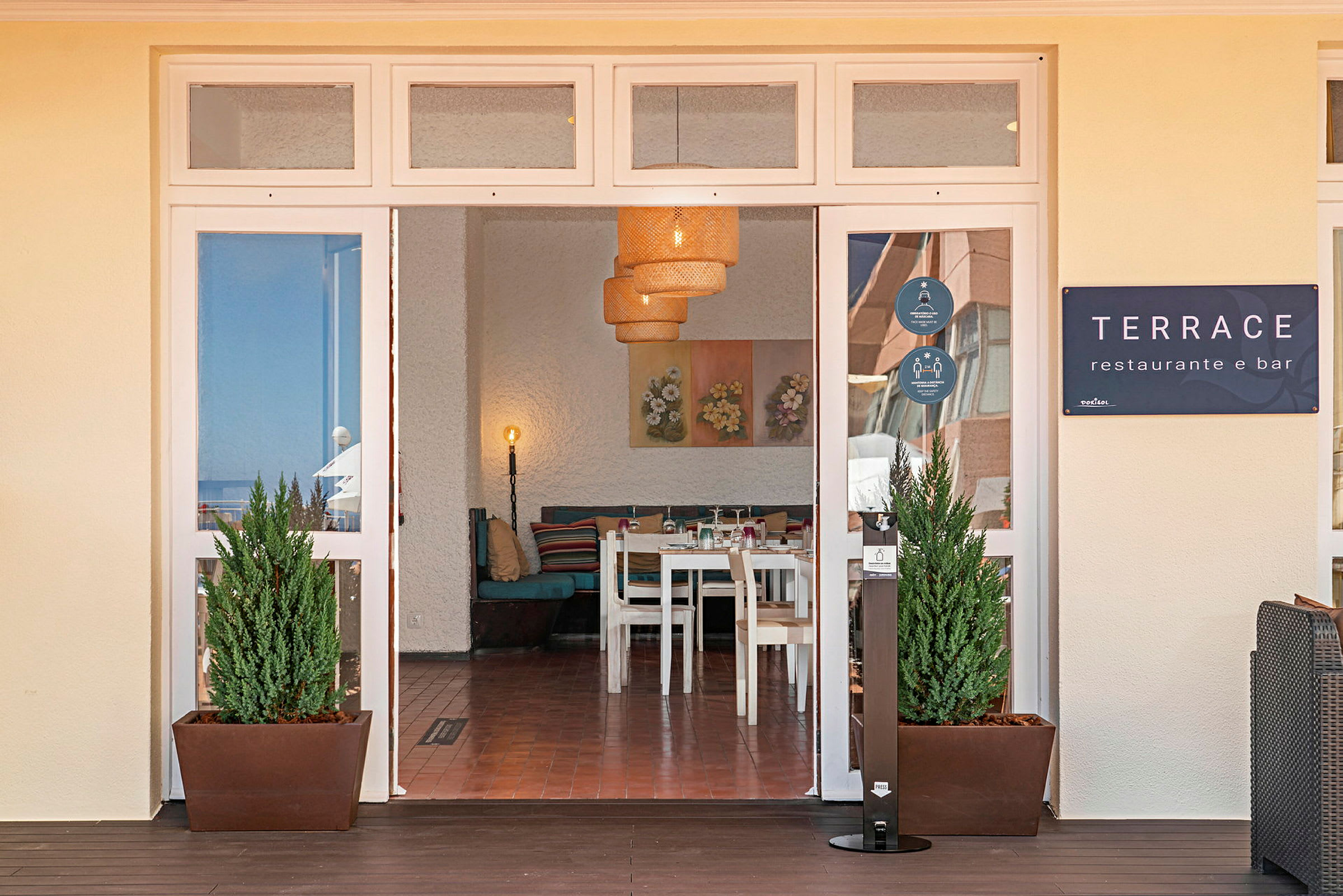 Inngangen til en restaurant med navnet Terrace, innendørs vises bord og stoler samt dekorerte vegger. (AI-generert tekst)