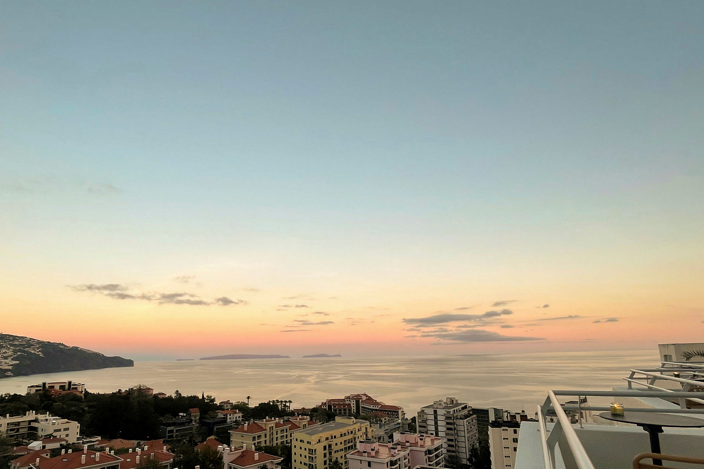 Bilde av en kystby med bygninger i forgrunnen og havet i bakgrunnen under solnedgang. (AI-generert tekst)