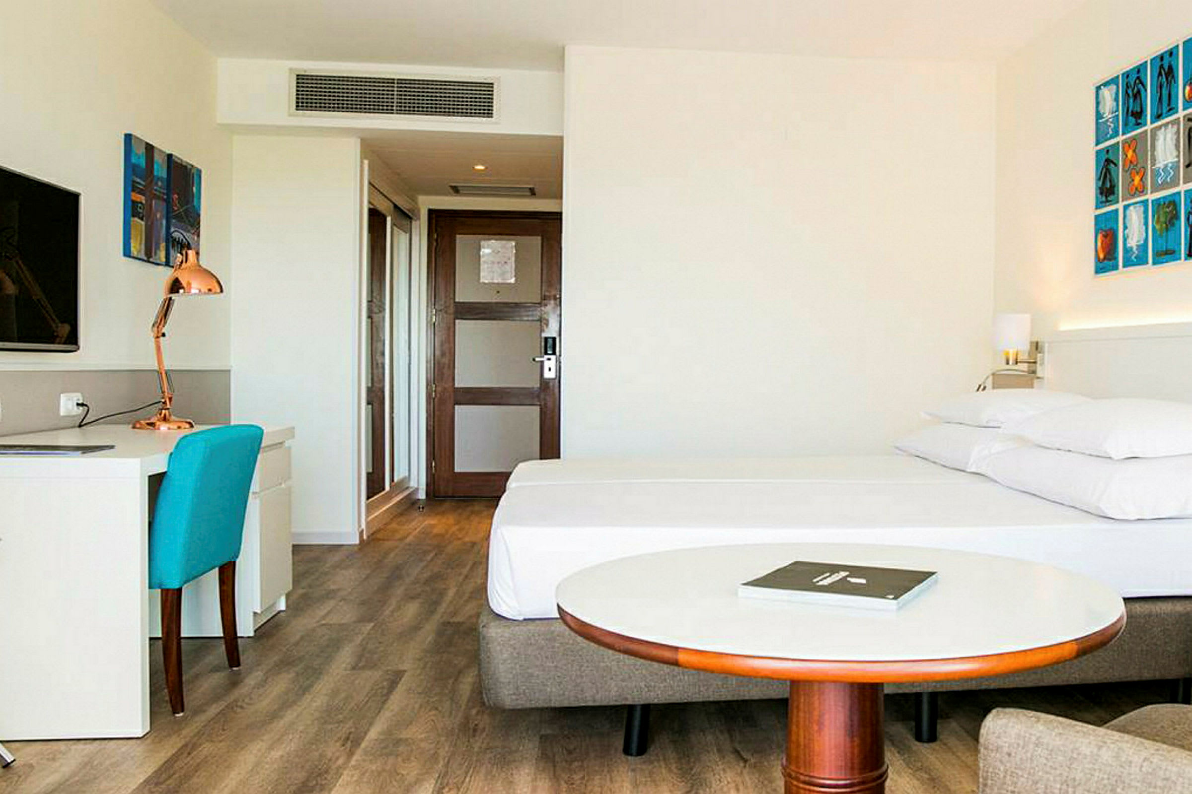 Hotellrom med en seng, skrivebord og stål, samt et rundt bord foran sengen. (AI-generert tekst)