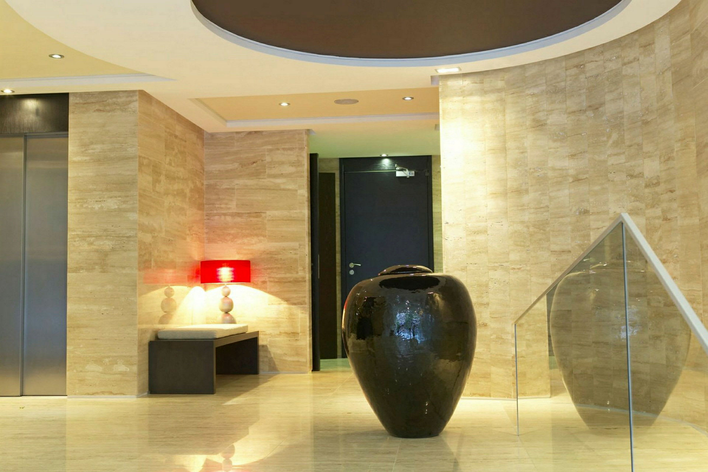 En hotellobby med en stor svart dekorativ vase i forgrunnen, omgitt av marmordetaljer og moderne design. (AI-generert tekst)