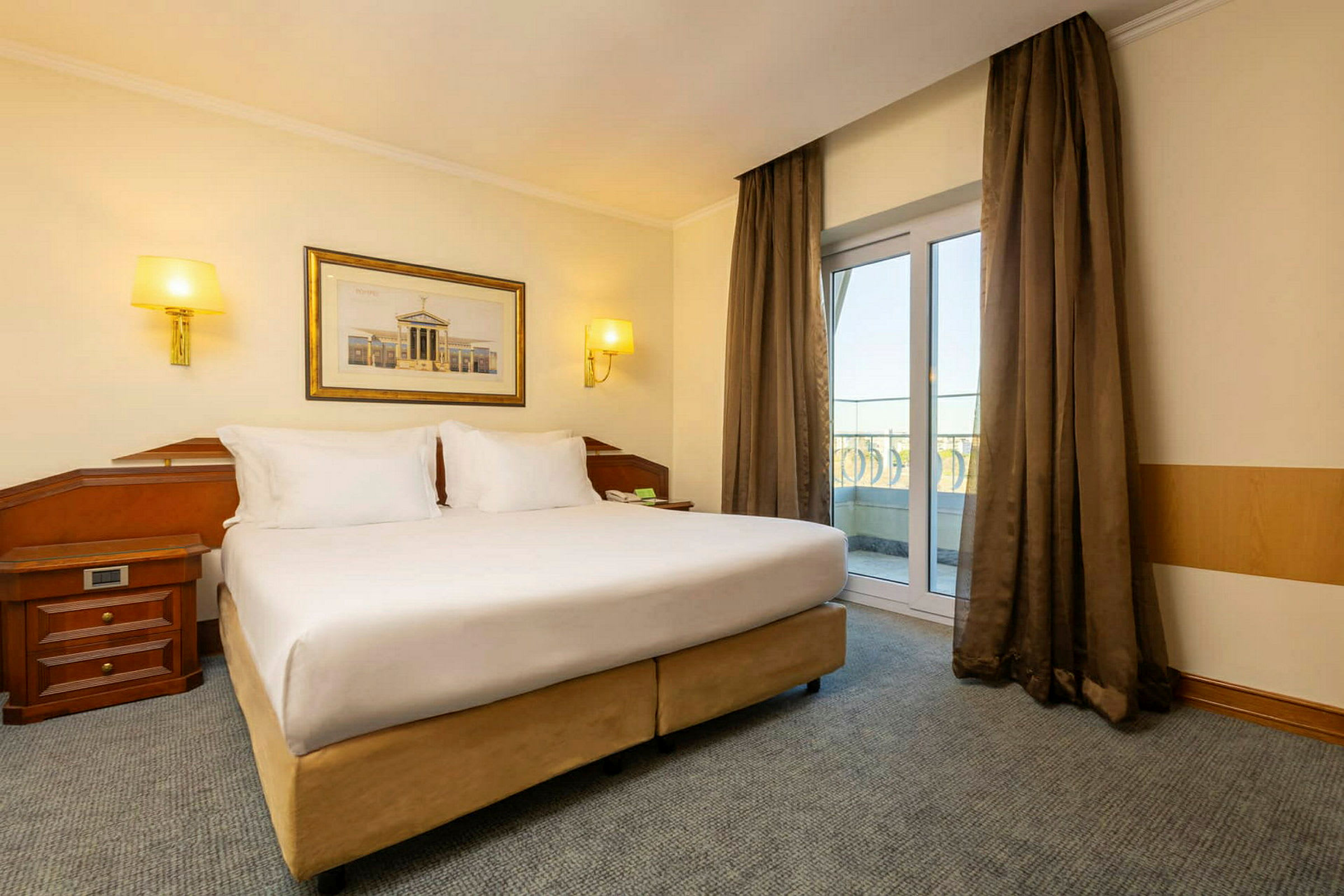 Et hotellrom med en stor dobbeltseng og vinduer som vender mot balkongen. (AI-generert tekst)