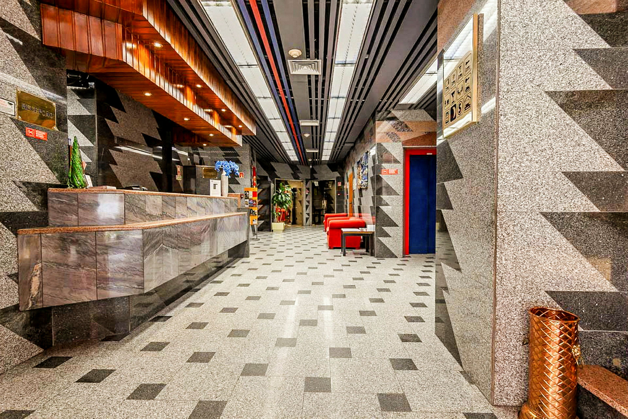 Hotellobby med marmordekor, et resepsjonsområde og røde sittemøbler. (AI-generert tekst)