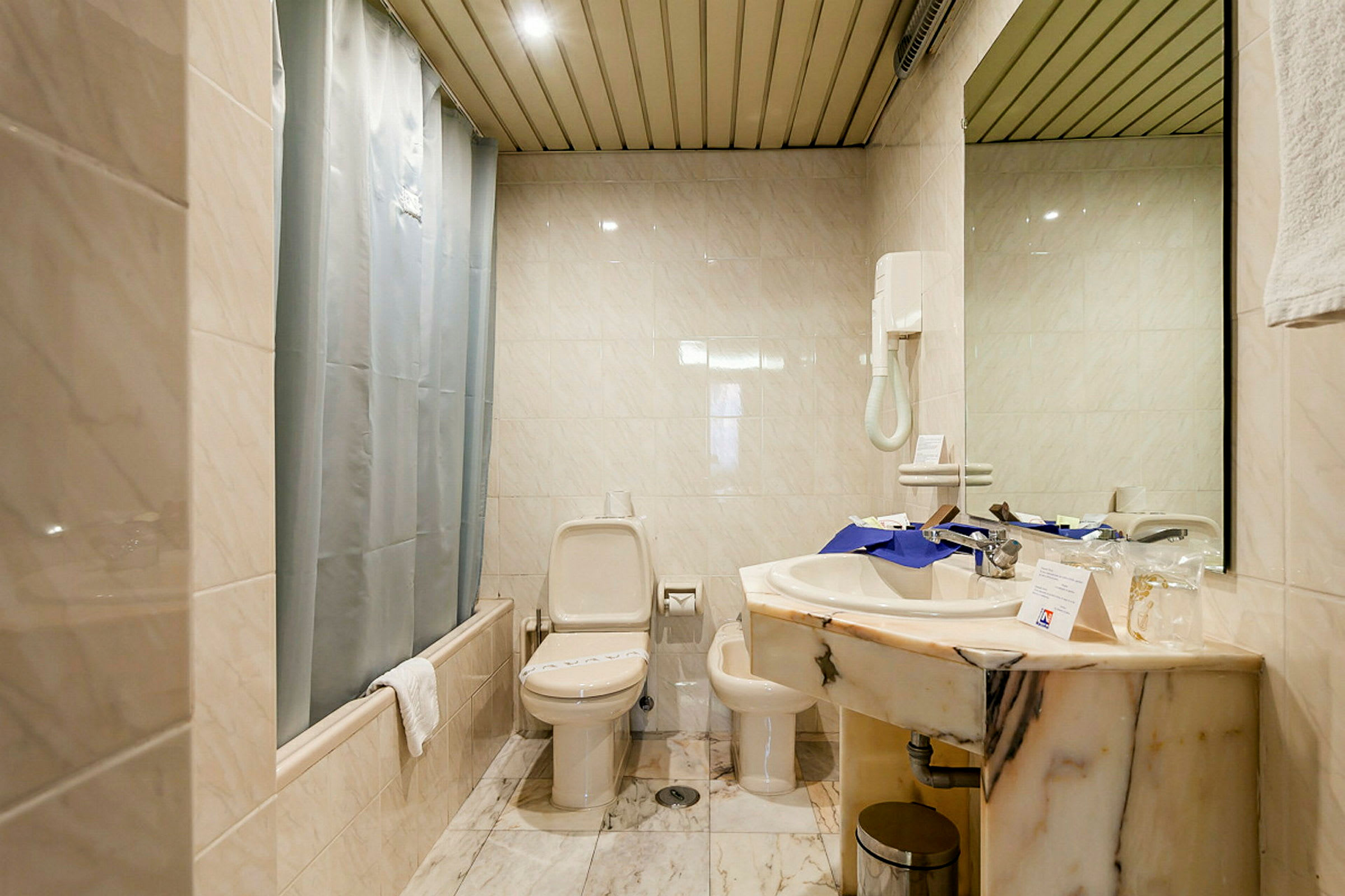 Et bad med toalett, bidet og vask. Fliser på vegger og gulv samt en dusj med forheng. (AI-generert tekst)