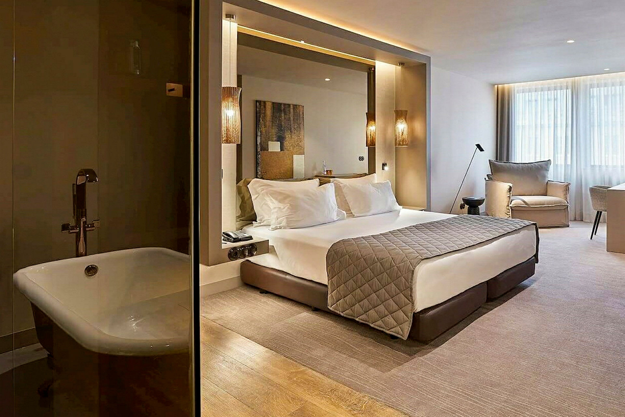 Et moderne hotellrom med en stor seng, sittemøbler og vinduer. Til venstre vises et badekar. (AI-generert tekst)