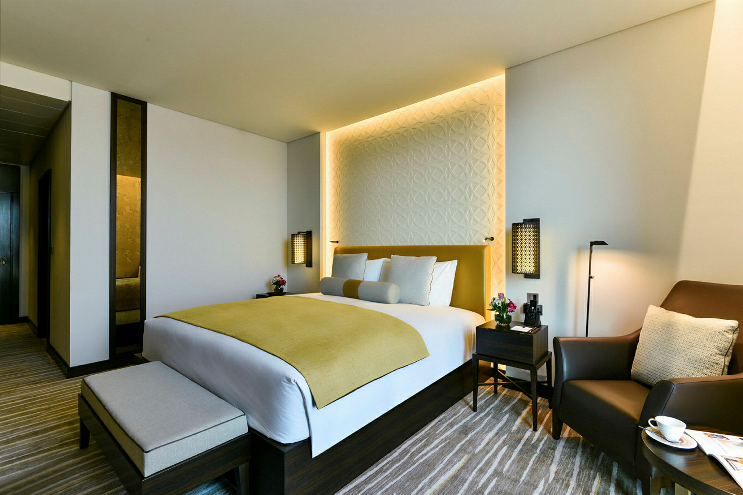 Et moderne hotellrom med en dobbeltseng, to nattbord og en komfortabel lenestol. (AI-generert tekst)