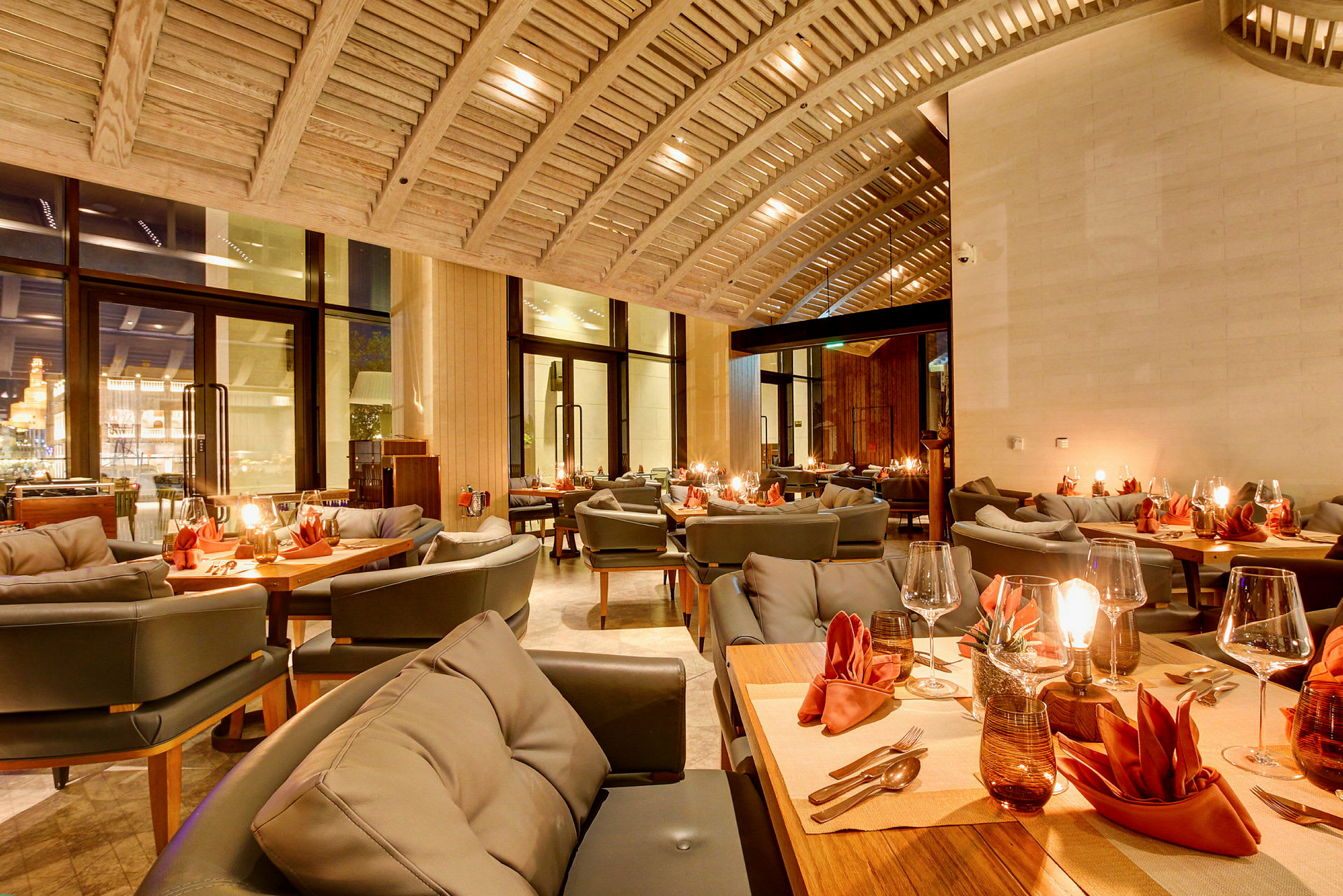 En elegant restaurant med bjelketak, dekkede bord med oransje servietter og koselig belysning. (AI-generert tekst)