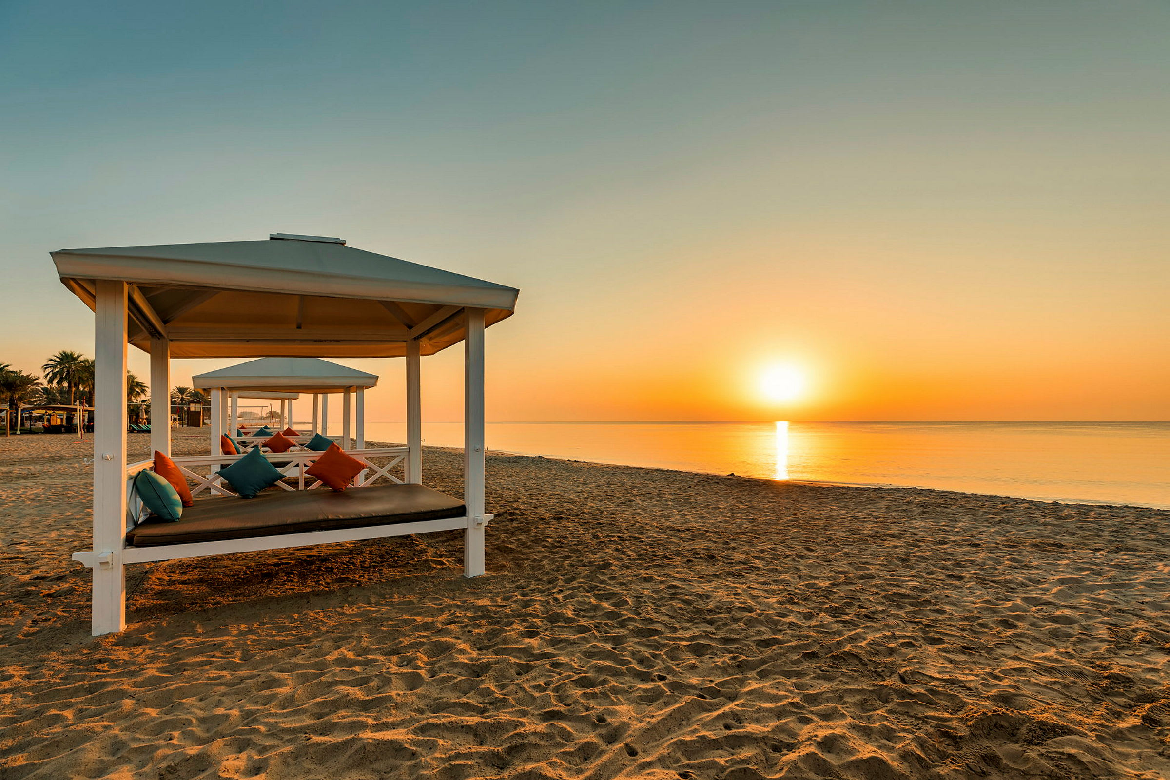Strand med hvite paviljonger og fargerike puter i solnedgangen. (AI-generert tekst)