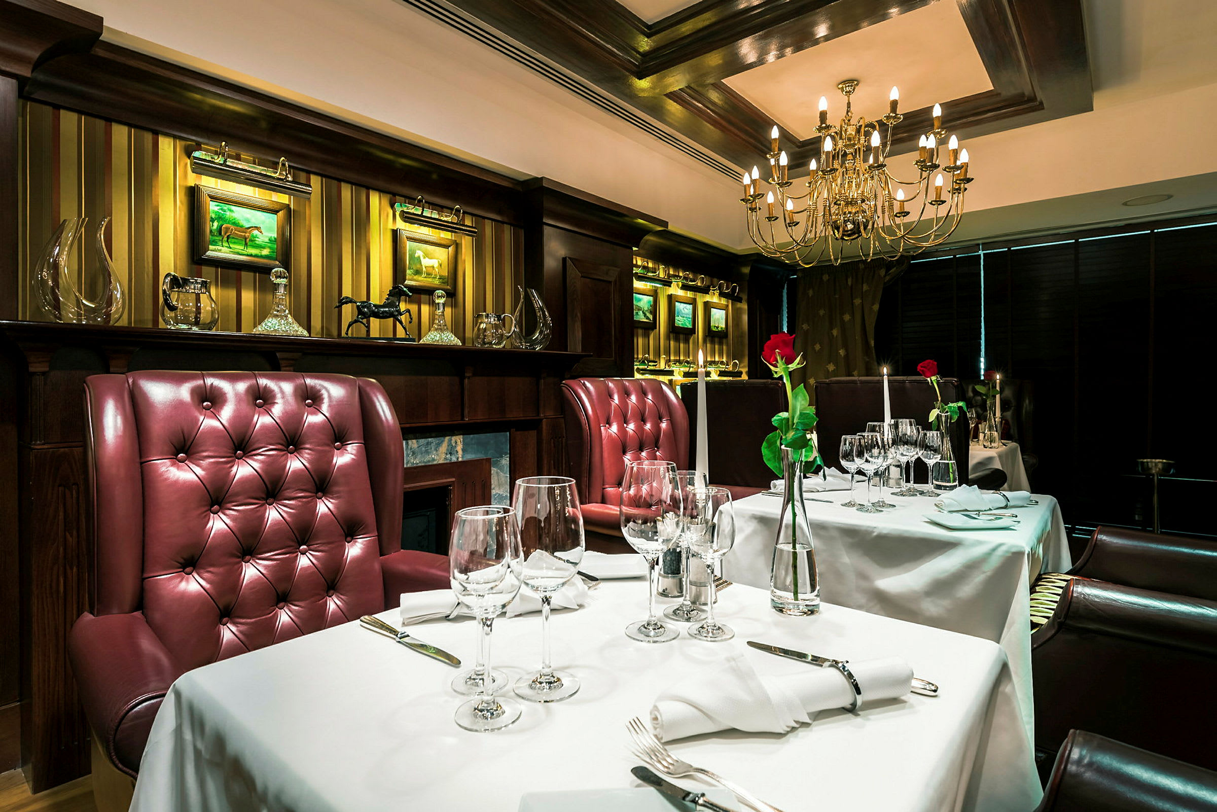 En elegant restaurantmiljø med bord dekket med hvite duker, røde polstrede stoler og lysekrone i taket. (AI-generert tekst)