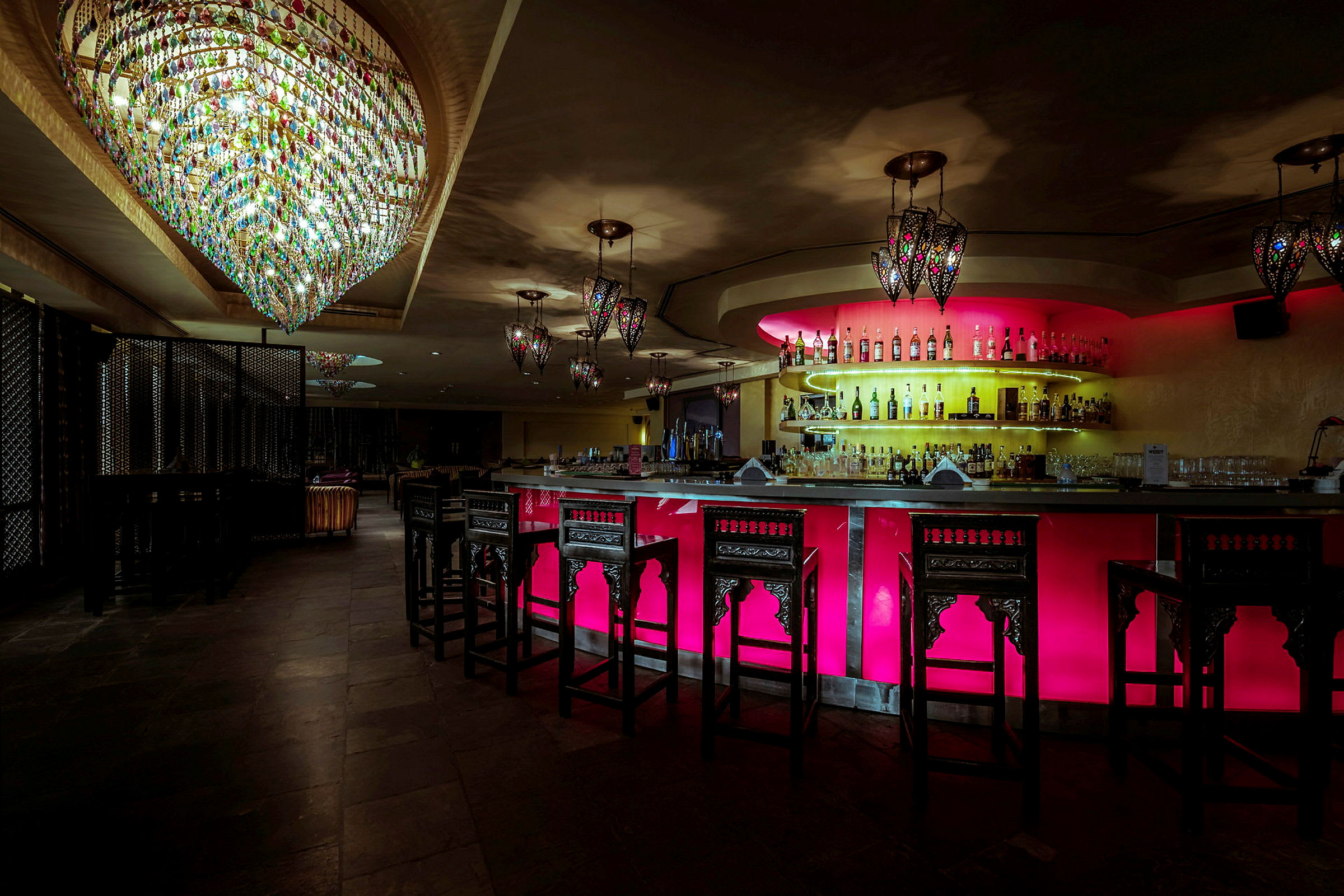 En elegant bar med opplyst bardisk i fargerike toner og lysekroner hengende fra taket. (AI-generert tekst)