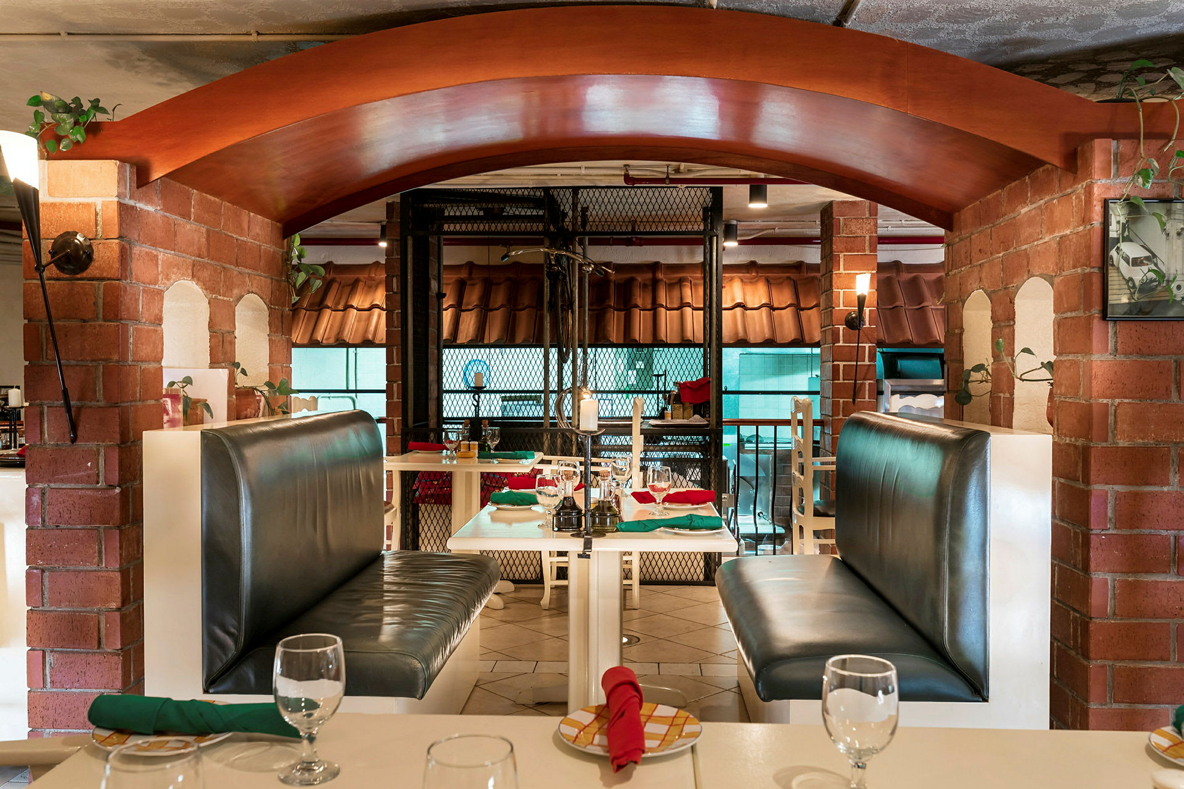 Interiør av en restaurant med bord og båser med skinnsofaer samt røde og grønne servietter. (AI-generert tekst)