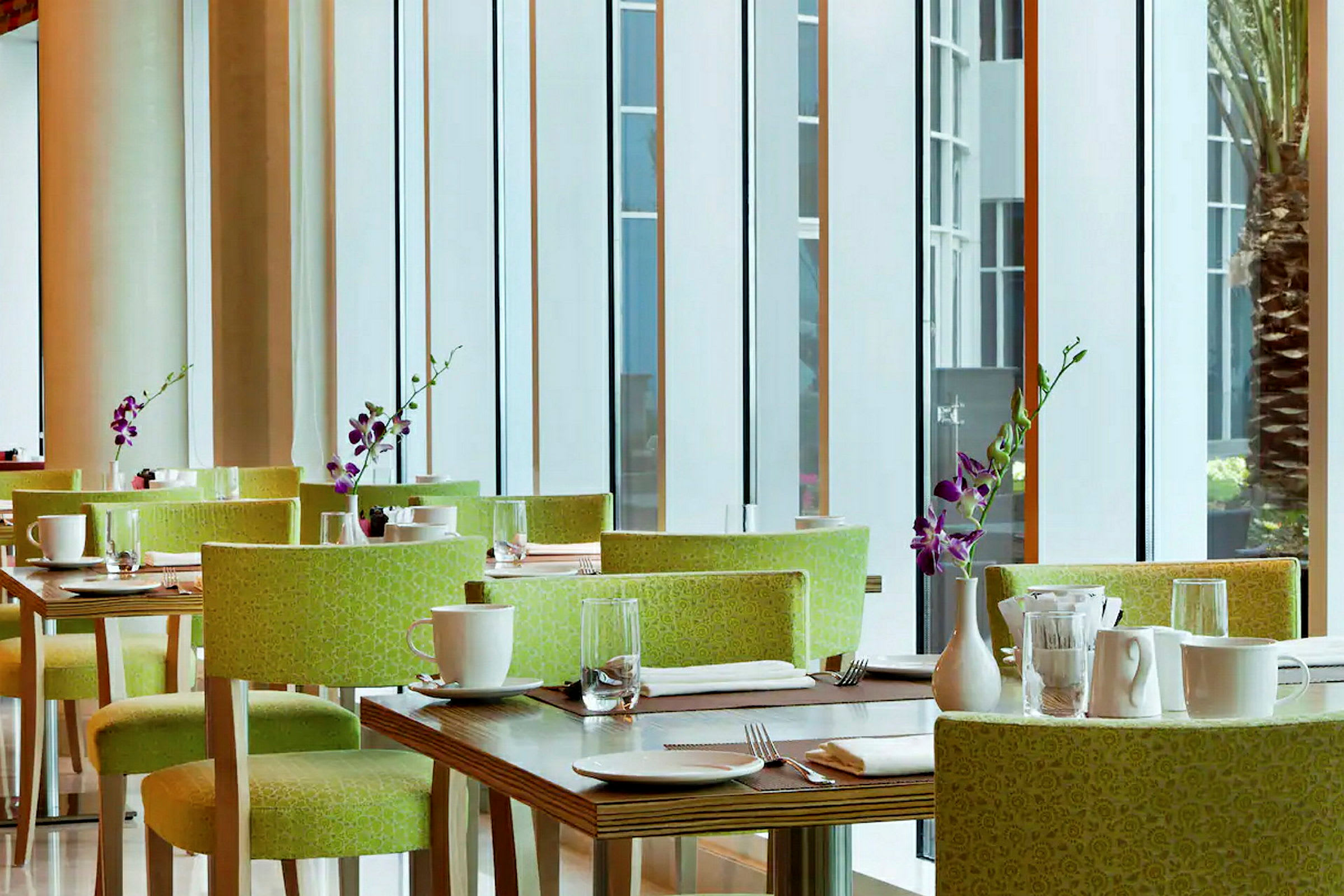 Et moderne restaurantområde med grønne stoler, dekkede bord, hvite kopper og lilla orkidévaser. (AI-generert tekst)