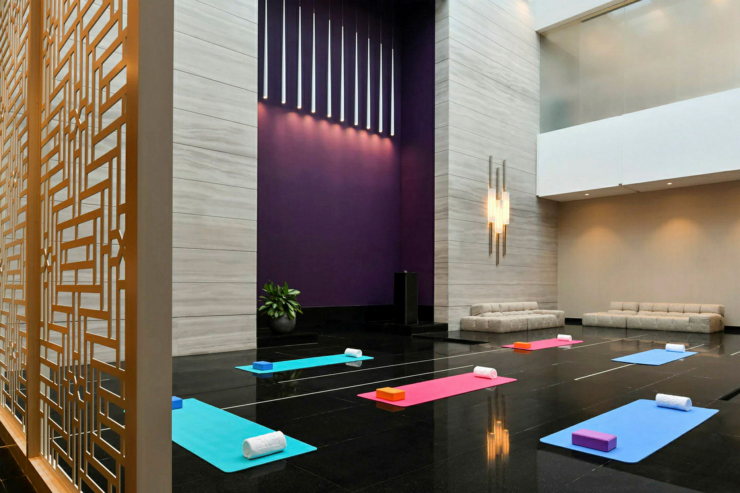 Et rom med yogamatter og tilhørende tilbehør plassert på et blankt gulv. Det er moderne sofaer på siden og en dekorativ avskjerming med gitter. (AI-generert tekst)