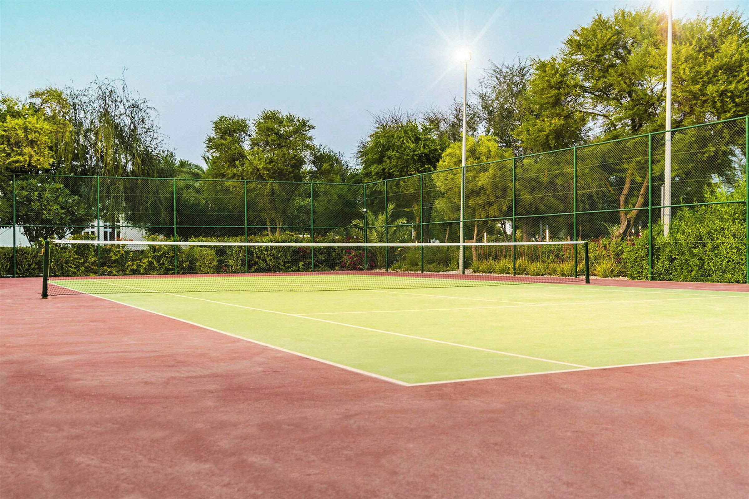 En tom tennisbane med nett og omgivelser fylt med grønt. (AI-generert tekst)
