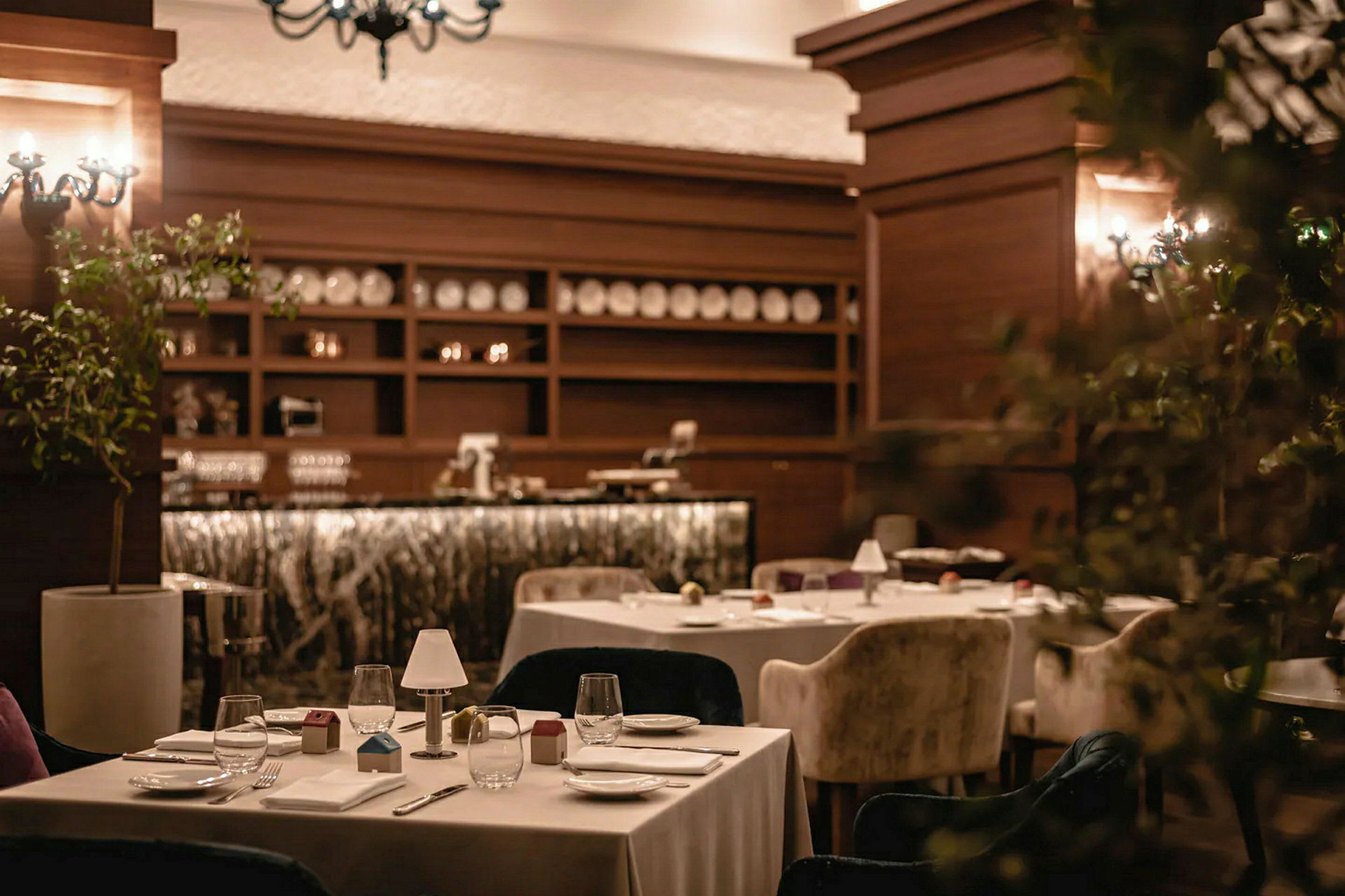 Et restaurantinteriør med dekkede bord og komfortable stoler, omgitt av varm belysning og tredekorer. (AI-generert tekst)