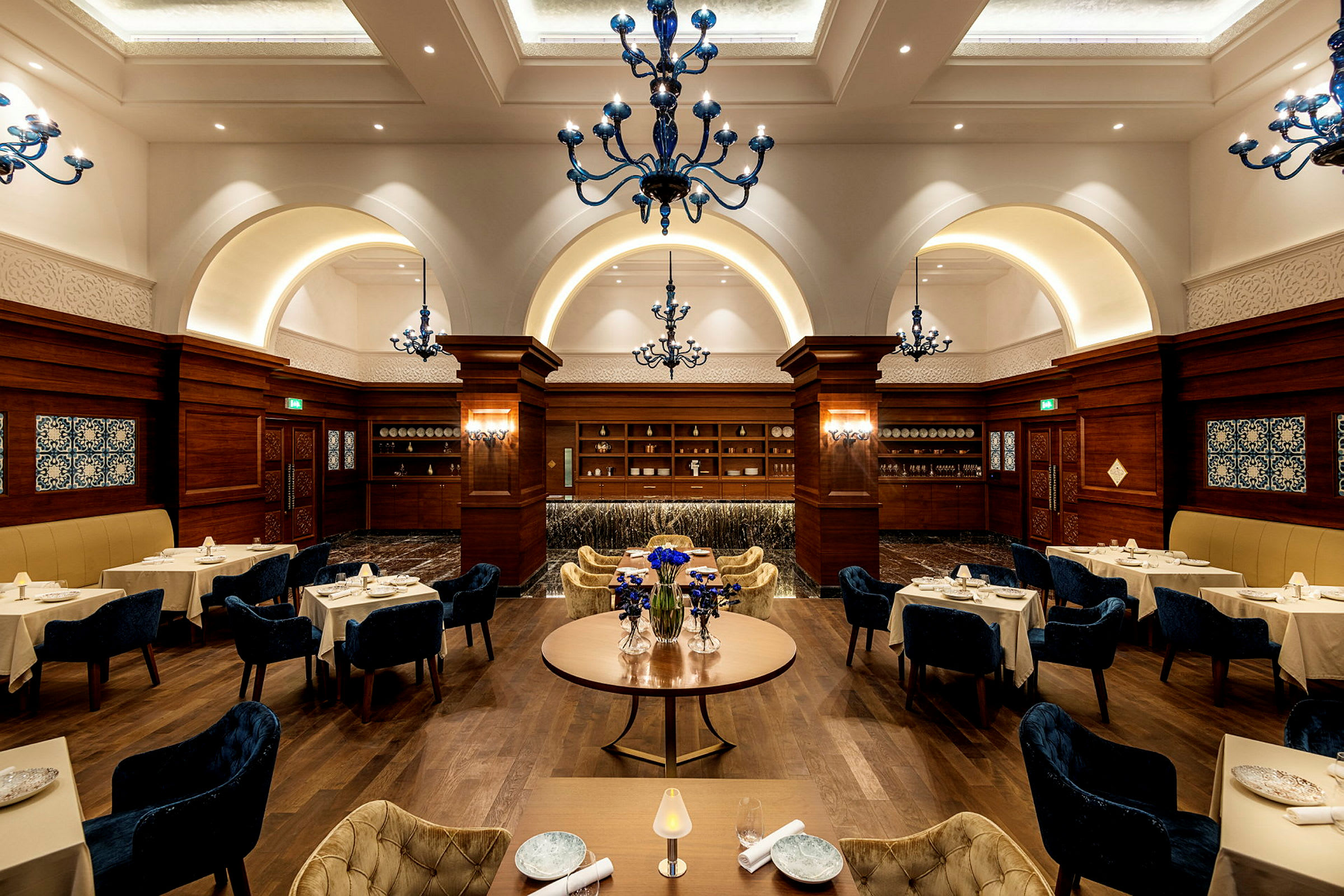 Interiør av en elegant restaurant med dekkede bord og dekorerte blå lysekroner. (AI-generert tekst)