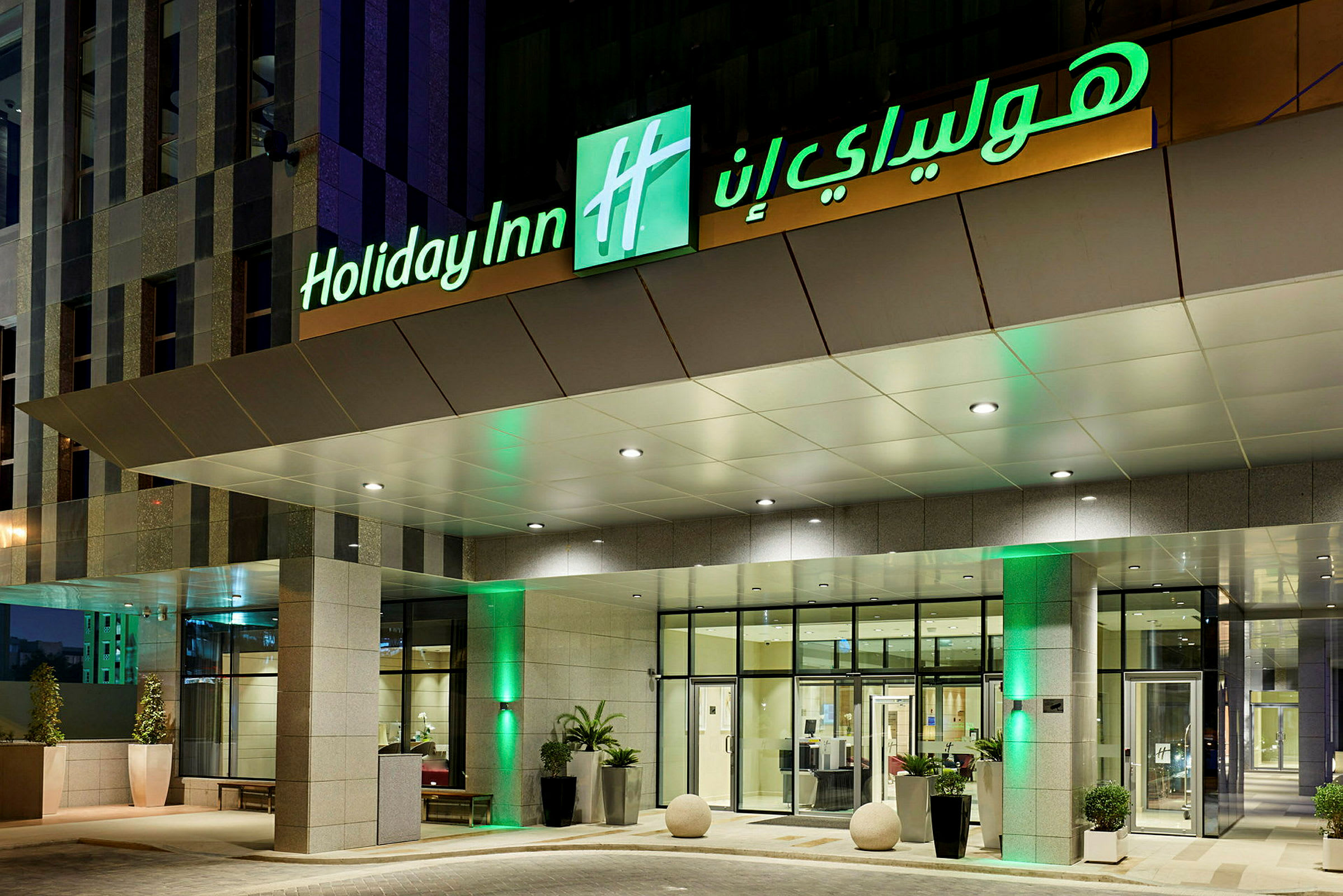 Inngangen til et hotell med skiltet 'Holiday Inn' som er opplyst. (AI-generert tekst)