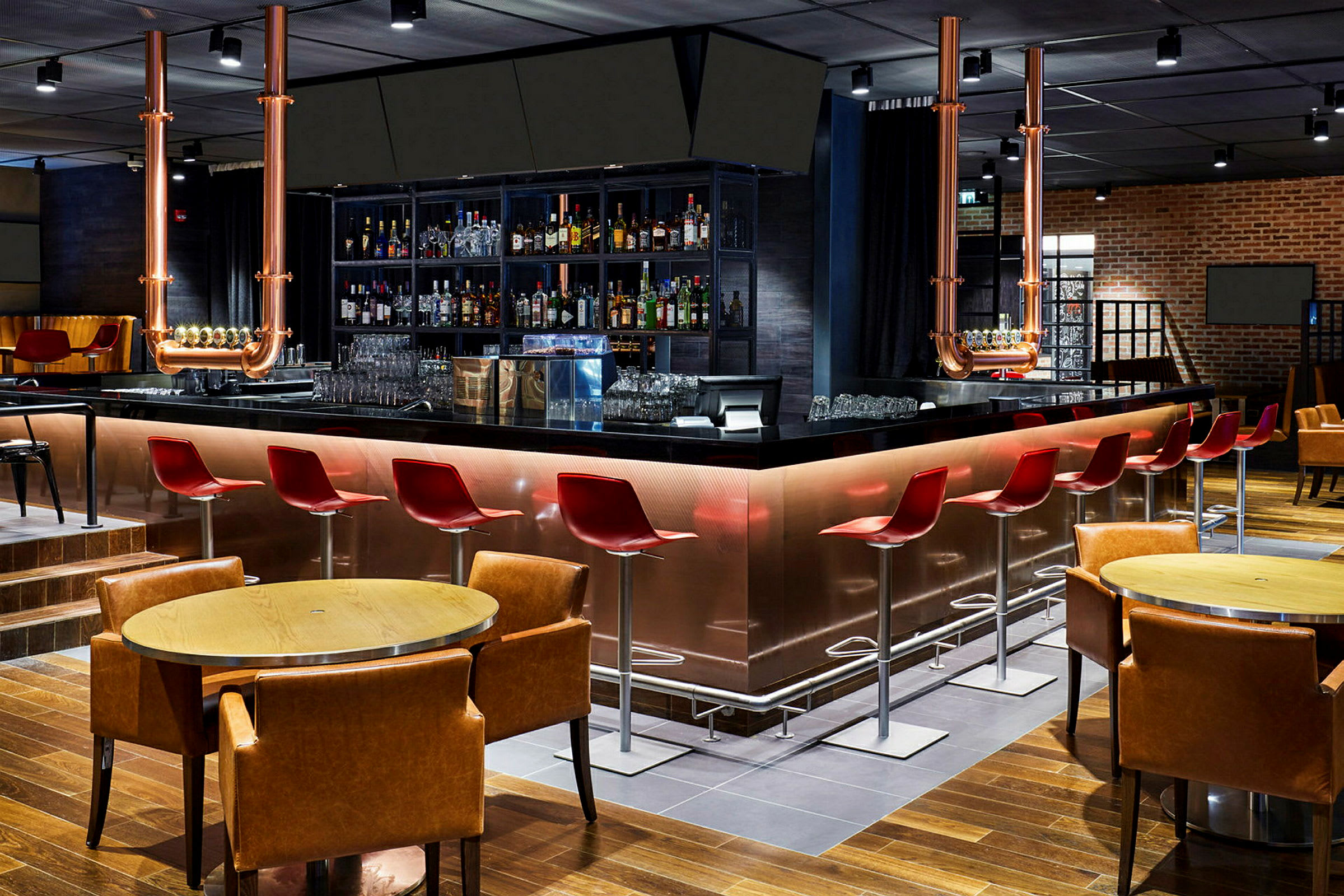 En moderne bar med røde stoler, en blank svart bardisk og en rekke flasker med alkohol på hyllene bak. (AI-generert tekst)