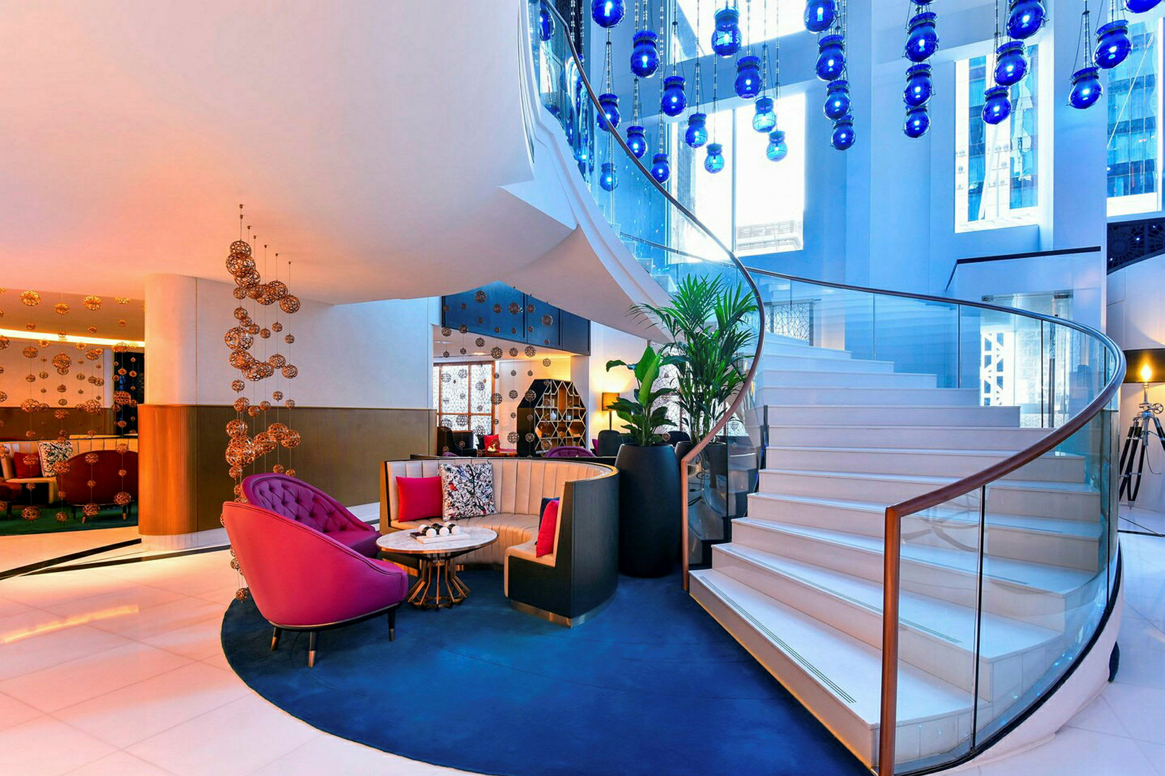 Lys og elegant hotellobby med spiraltrapp og dekorative blå lamper. (AI-generert tekst)