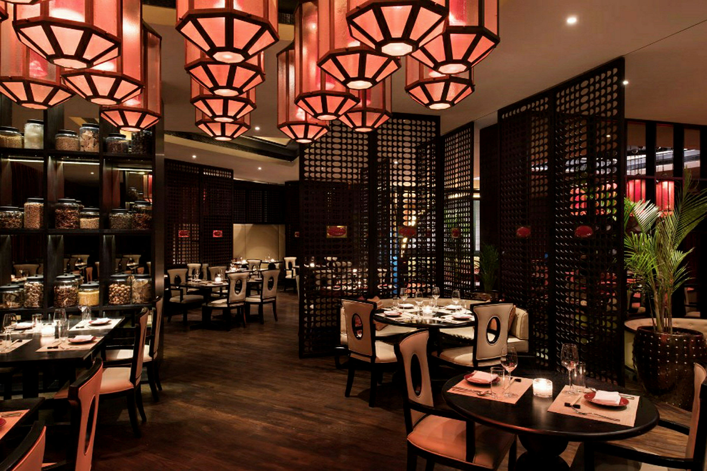 En restaurant med elegant interiør, bord med duker og stoler samt dekorative røde lamper i taket. (AI-generert tekst)