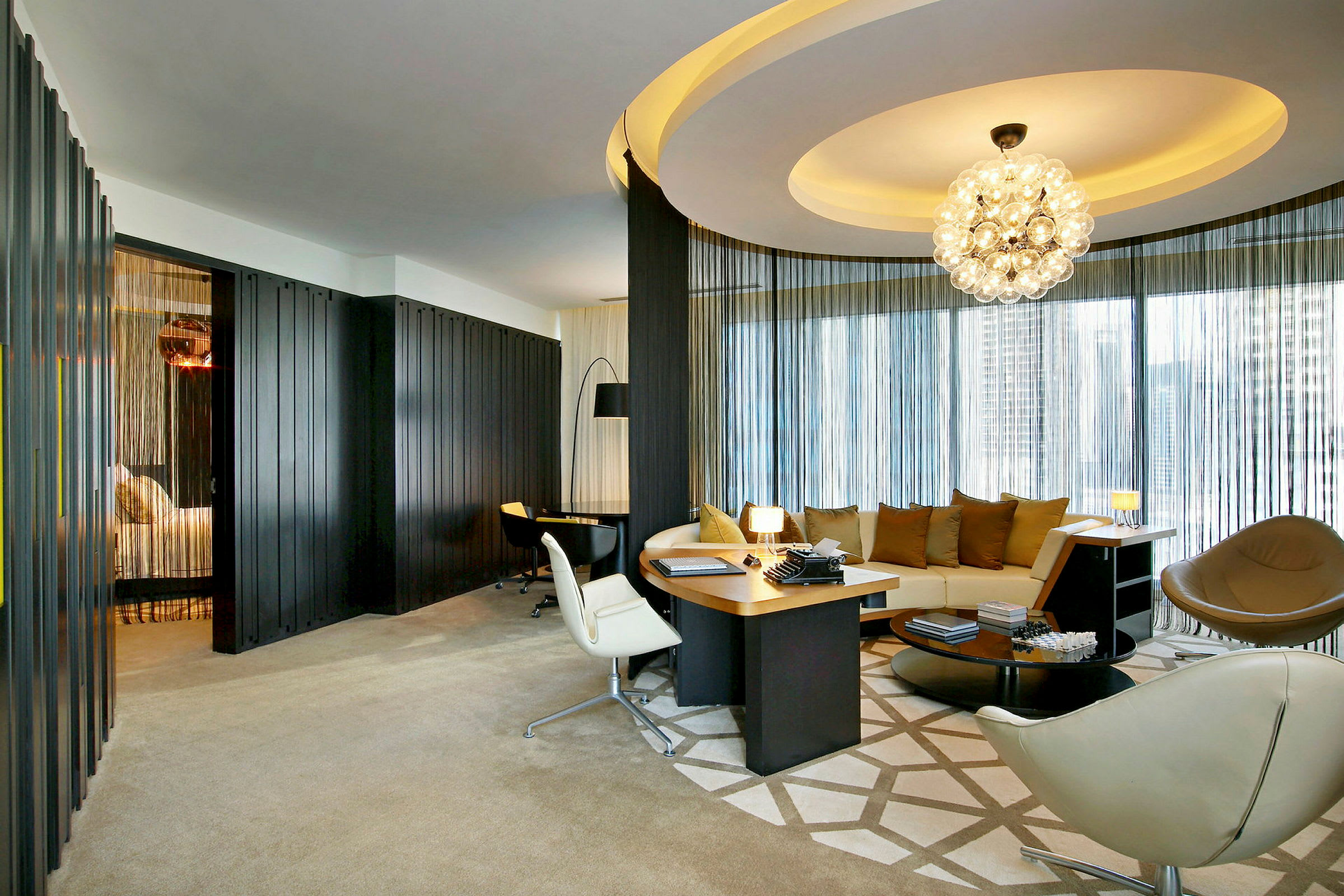 Et elegant hotellrom med moderne møbler, inkludert en rund sofa, skrivebord og dekorativ belysning. (AI-generert tekst)