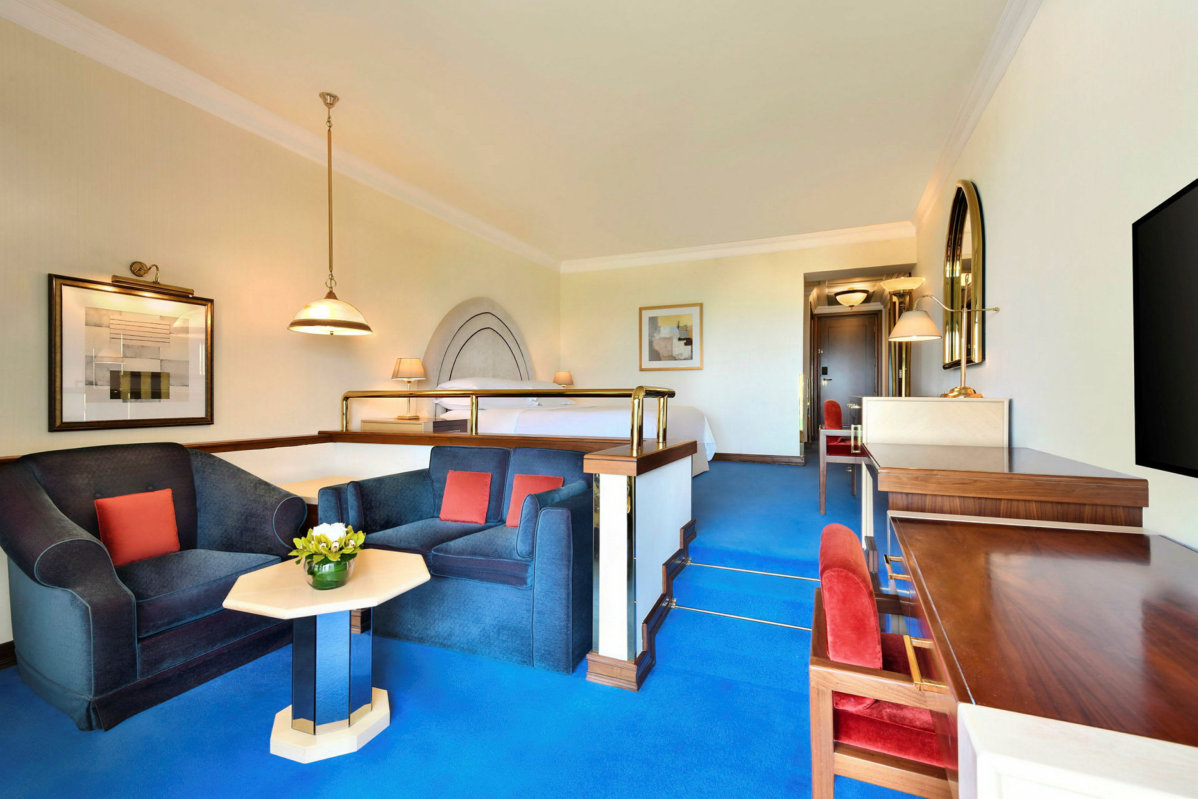 Et godt opplyst hotellrom med en forhøyet soveavdeling og en sittegruppe med to lenestoler og et lite bord. (AI-generert tekst)
