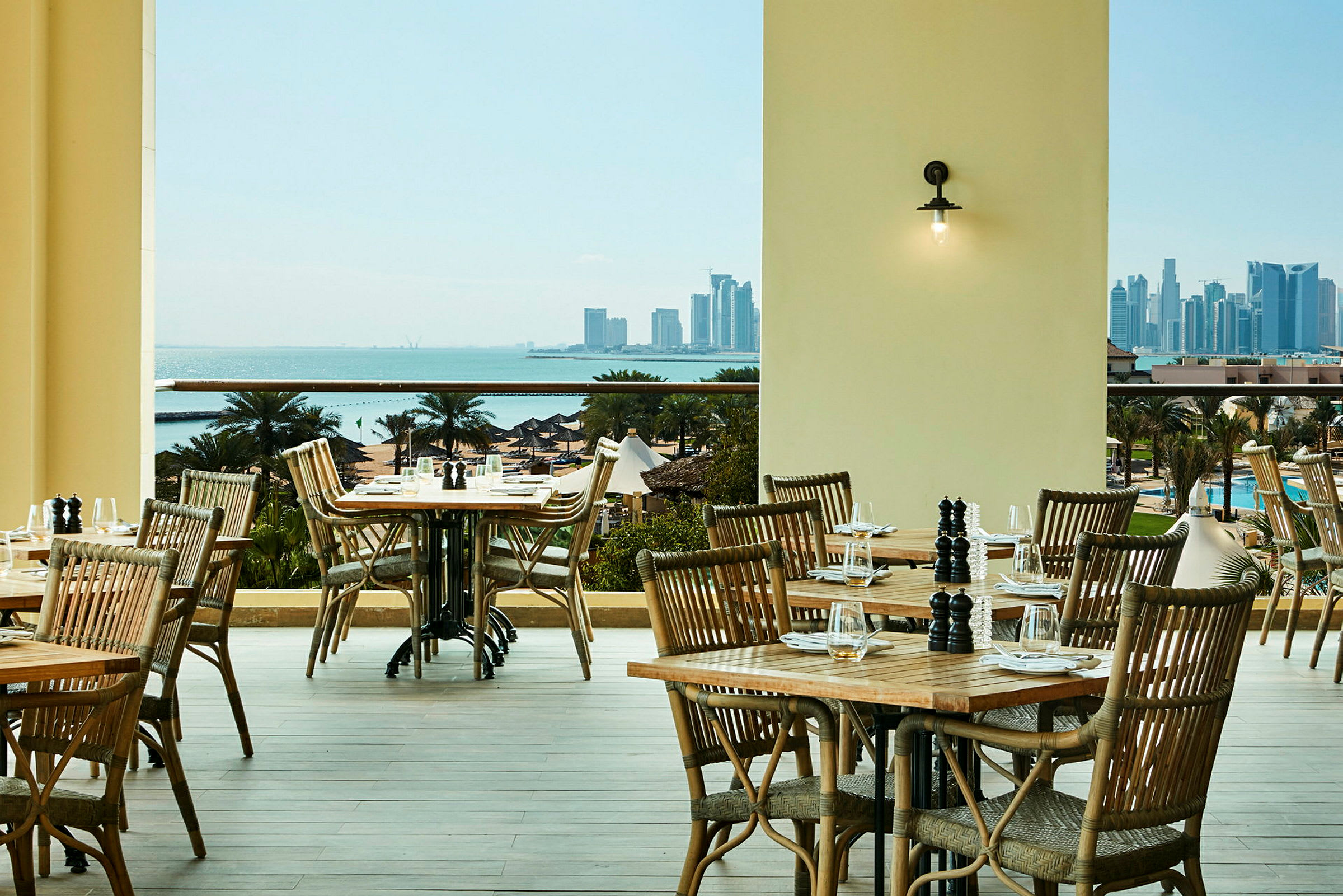 En restaurantterrasse med tremøbler med utsikt over havet og en bysilhuett. (AI-generert tekst)