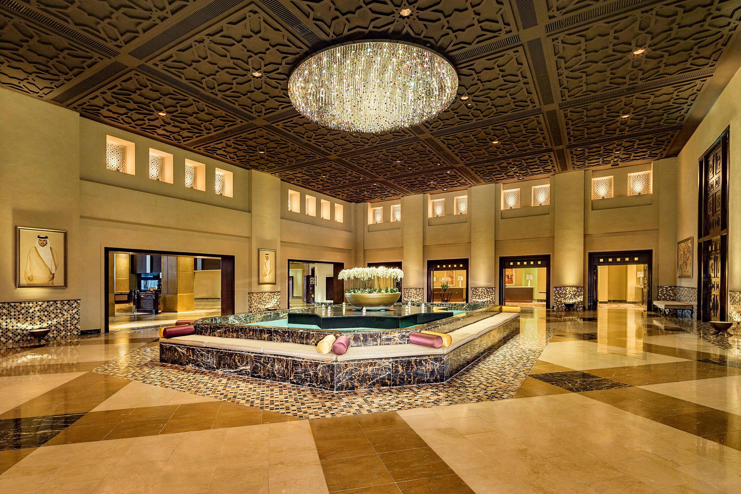 En elegant hotellobby med en stor lysekrone og et sentralt fonteneområde omgitt av sitteplasser. (AI-generert tekst)