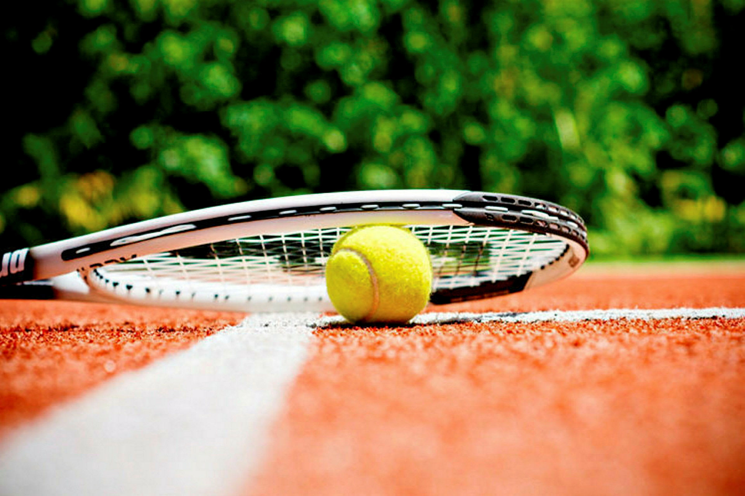 En tennisball og en racket ligger på en rød tennisbane nær en hvit linje. (AI-generert tekst)