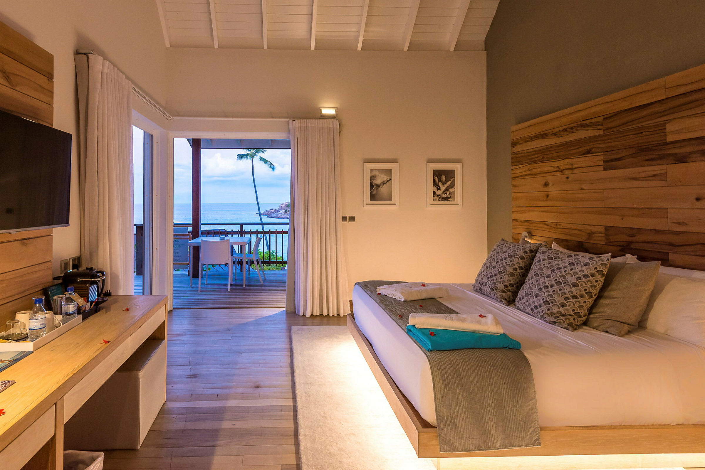 Et hotellrom med en stor seng og utgang til en terrasse med utsikt over havet. (AI-generert tekst)