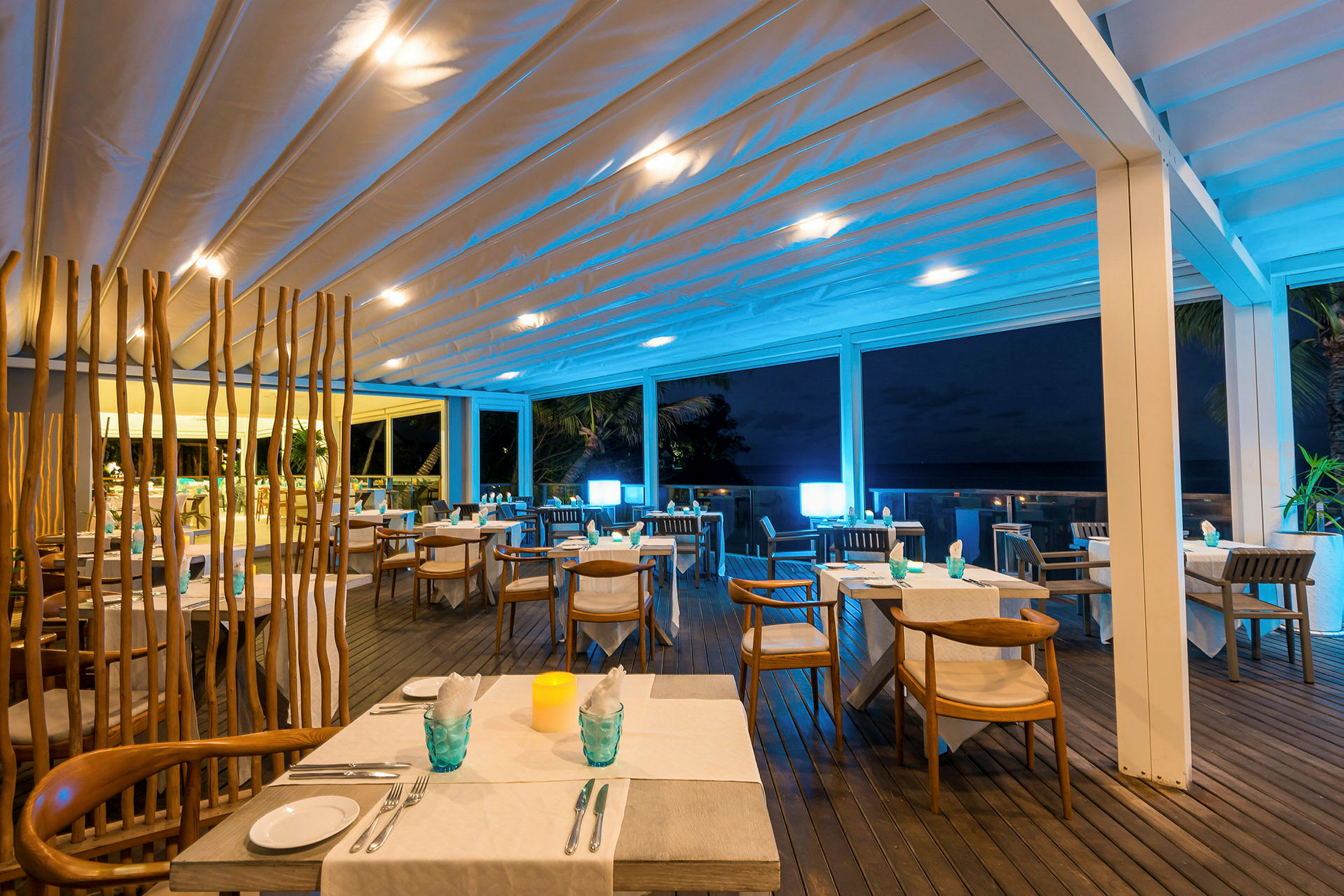 Dette er en opplyst restaurant med utendørsområde om kvelden, hvor det er bord og stoler med duker og lys. (AI-generert tekst)