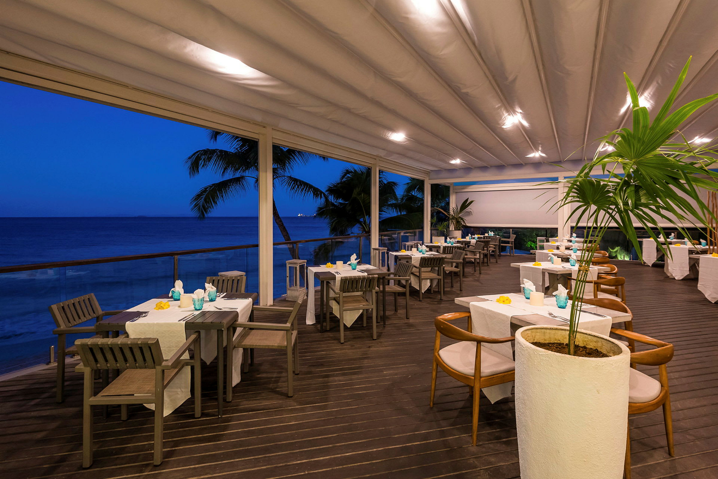 En uteservering ved havet med dekkede bord under en overbygd terrasse. (AI-generert tekst)