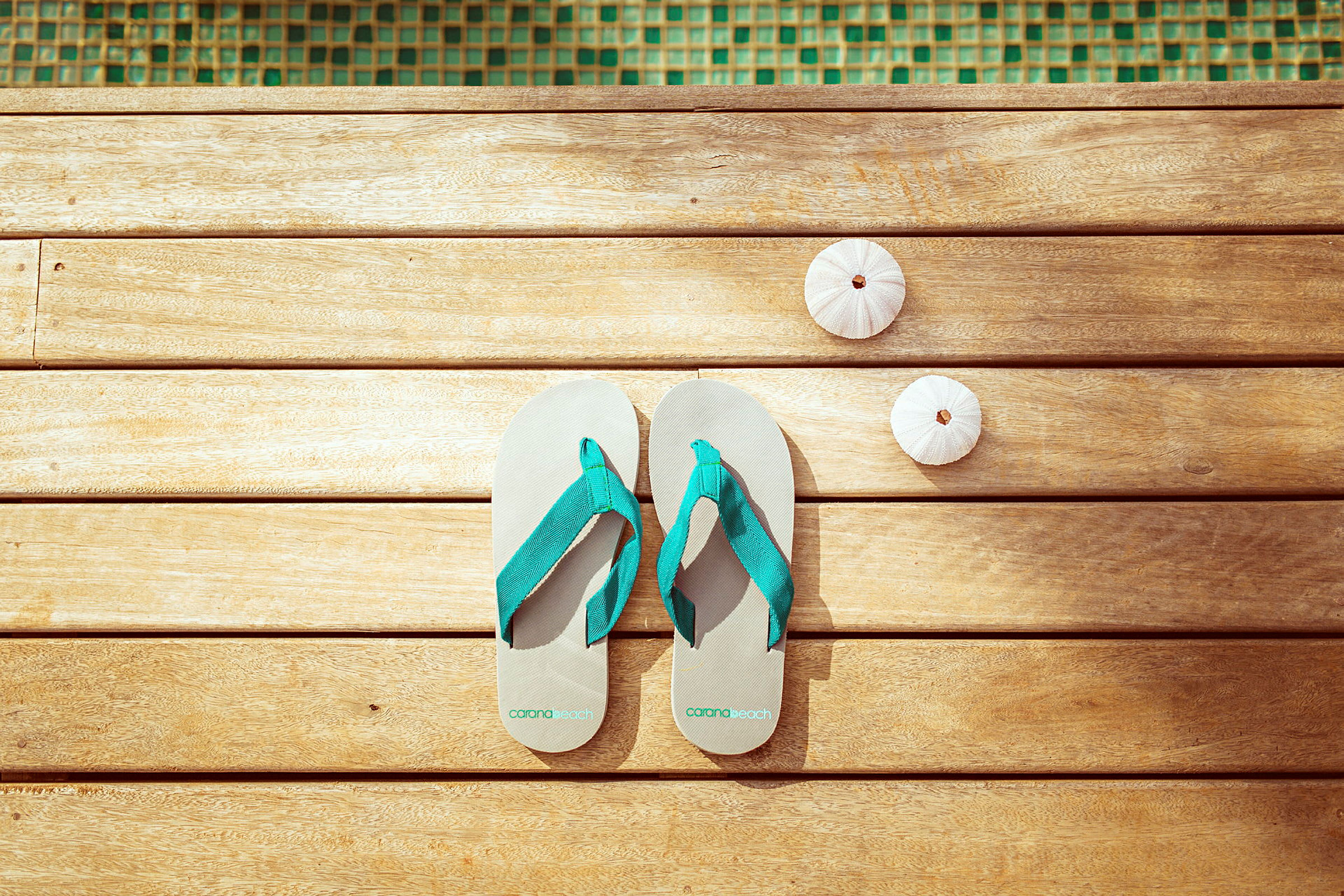 Et par flip-flops og to små hvite skjell ligger på en treoverflate nær et basseng. (AI-generert tekst)