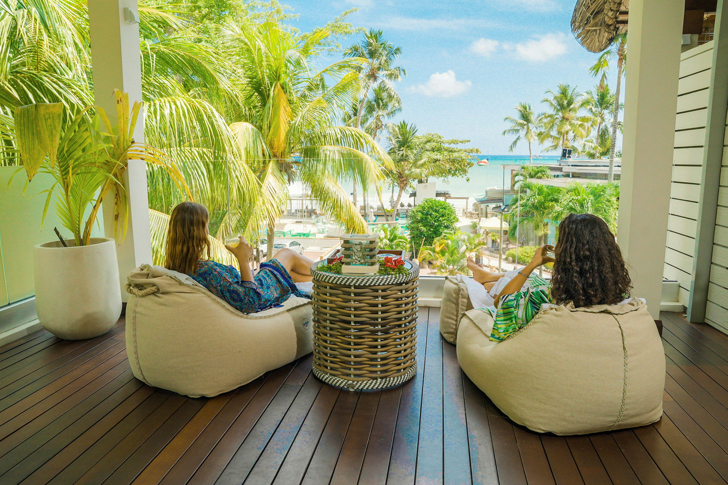 To personer sitter på puter på en terrasse med utsikt over palmer og havet. (AI-generert tekst)
