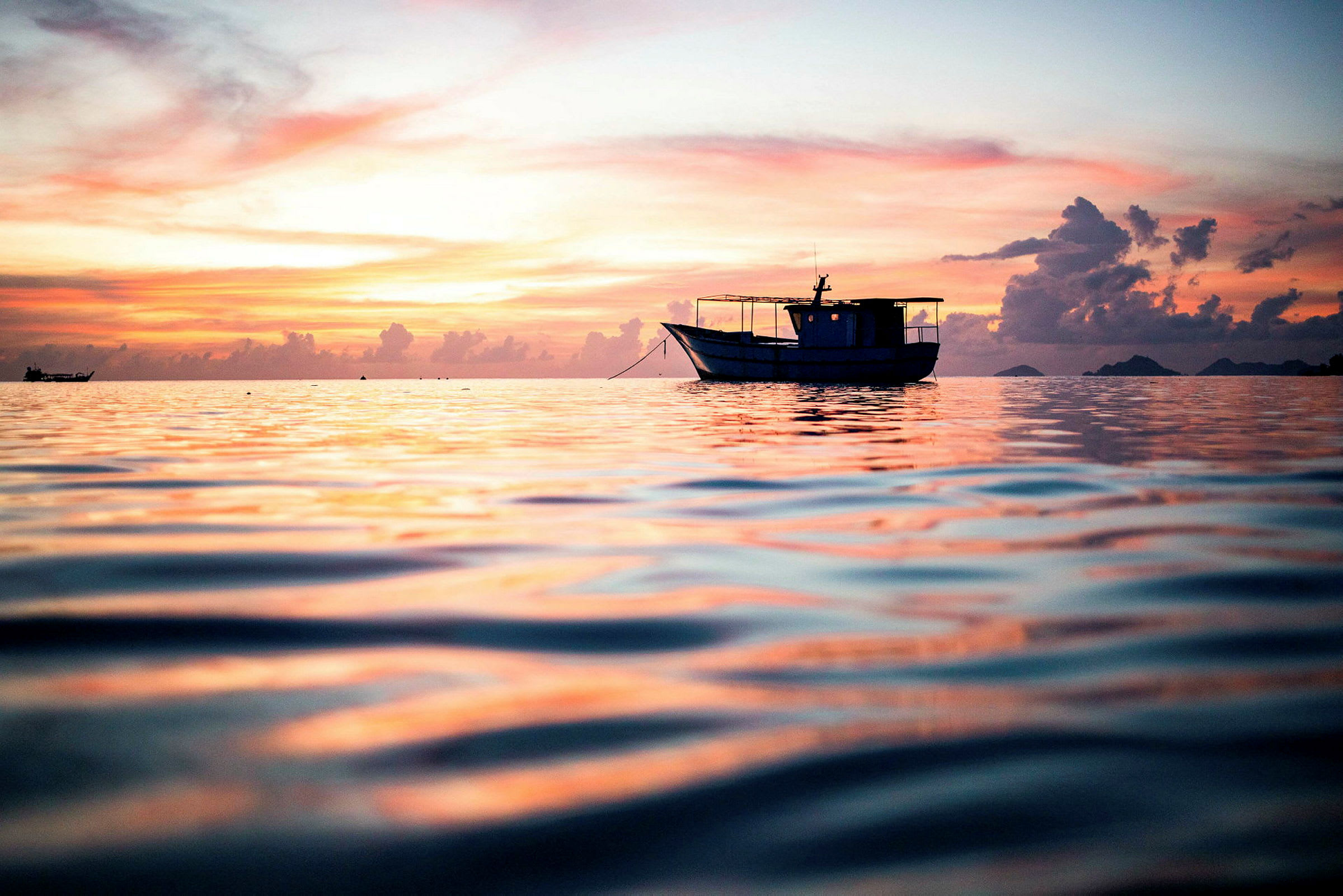 En båt flyter på havet under en fargerik solnedgang. (AI-generert tekst)