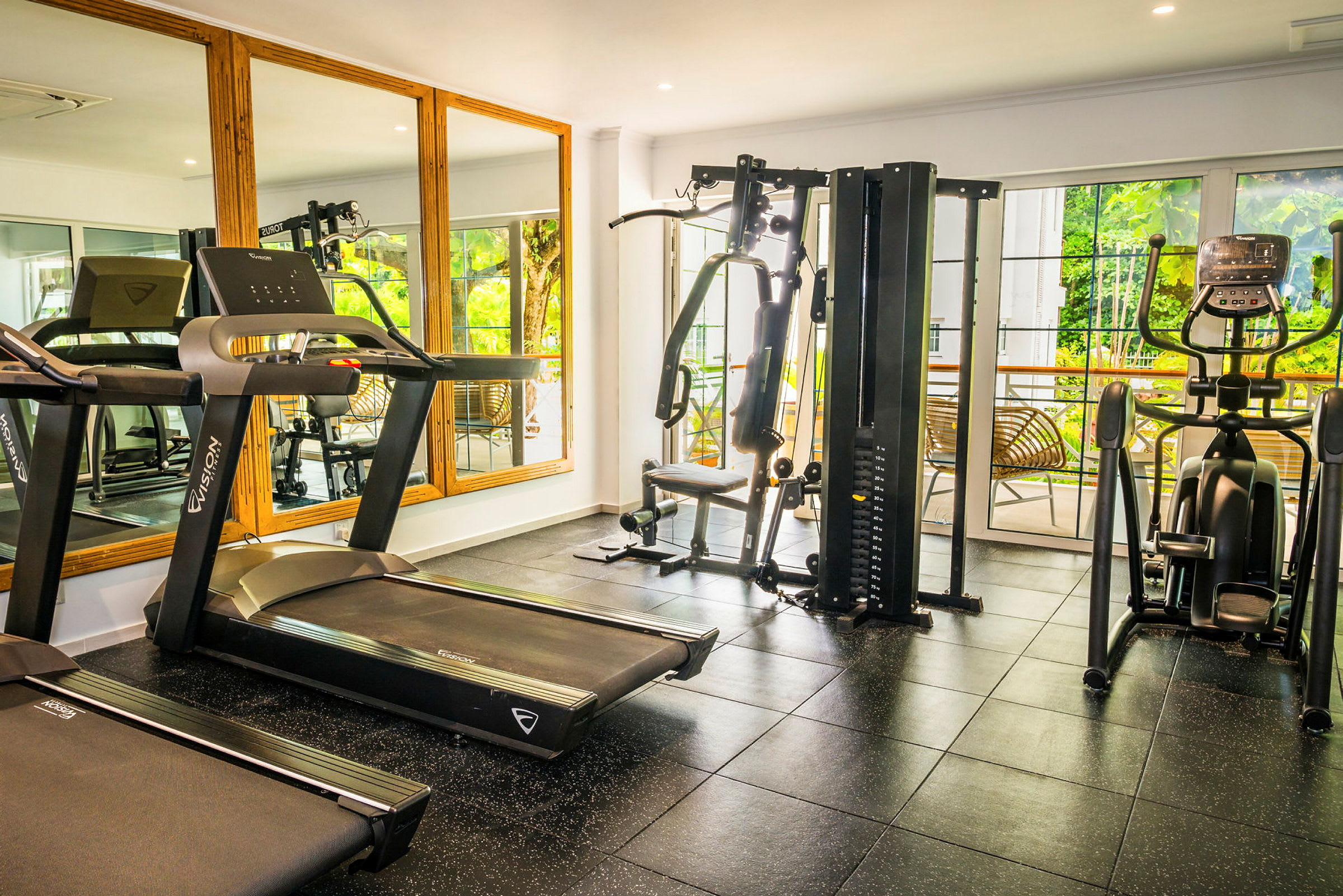 Et treningsstudio med forskjellige treningsmaskiner, inkludert tredemølle, multigym og treningssykkel. Bak treningsmaskinene er det store vinduer og speil. (AI-generert tekst)
