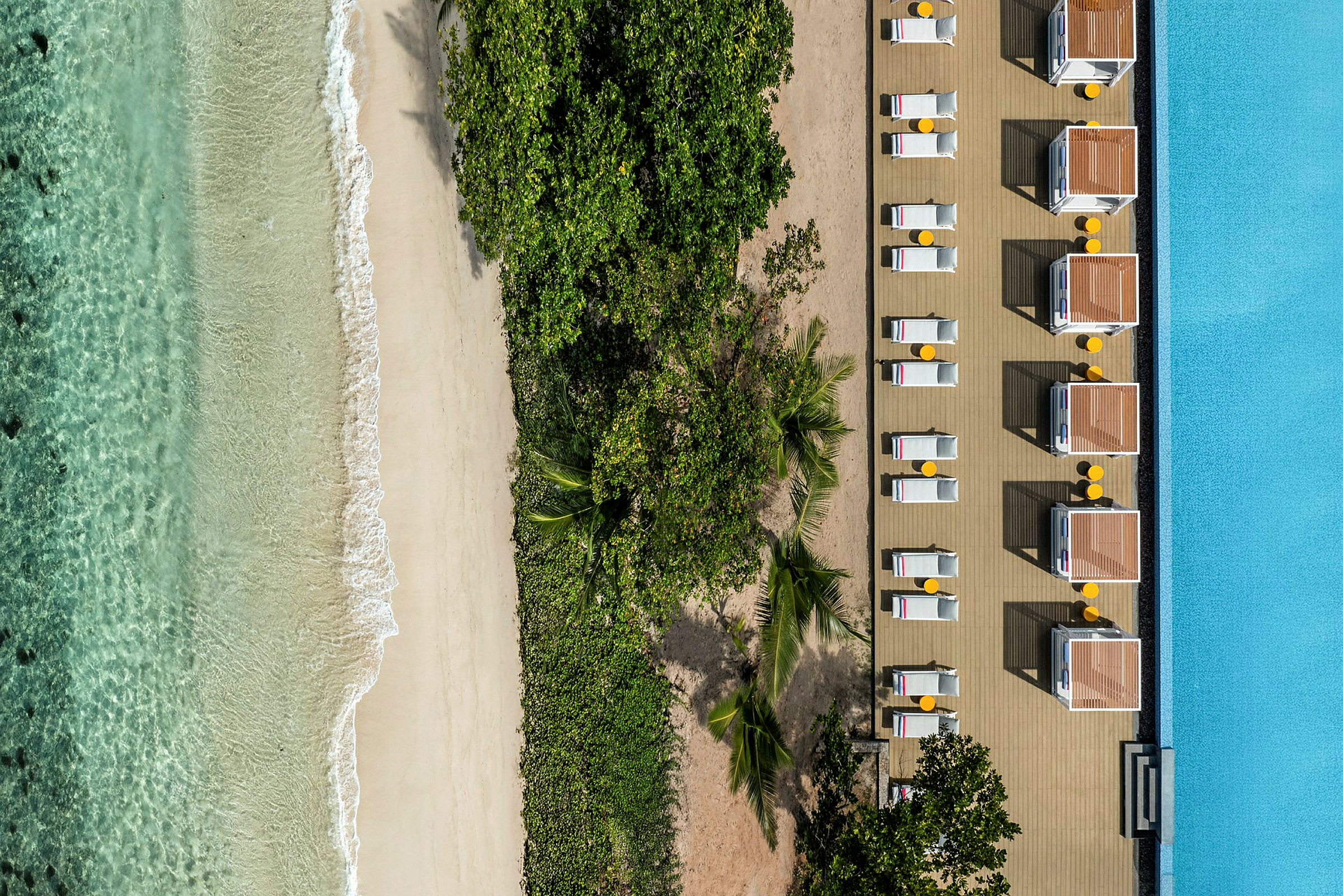 Dronefoto av strand med klart vann, vegetasjon og solsenger ved et basseng. (AI-generert tekst)