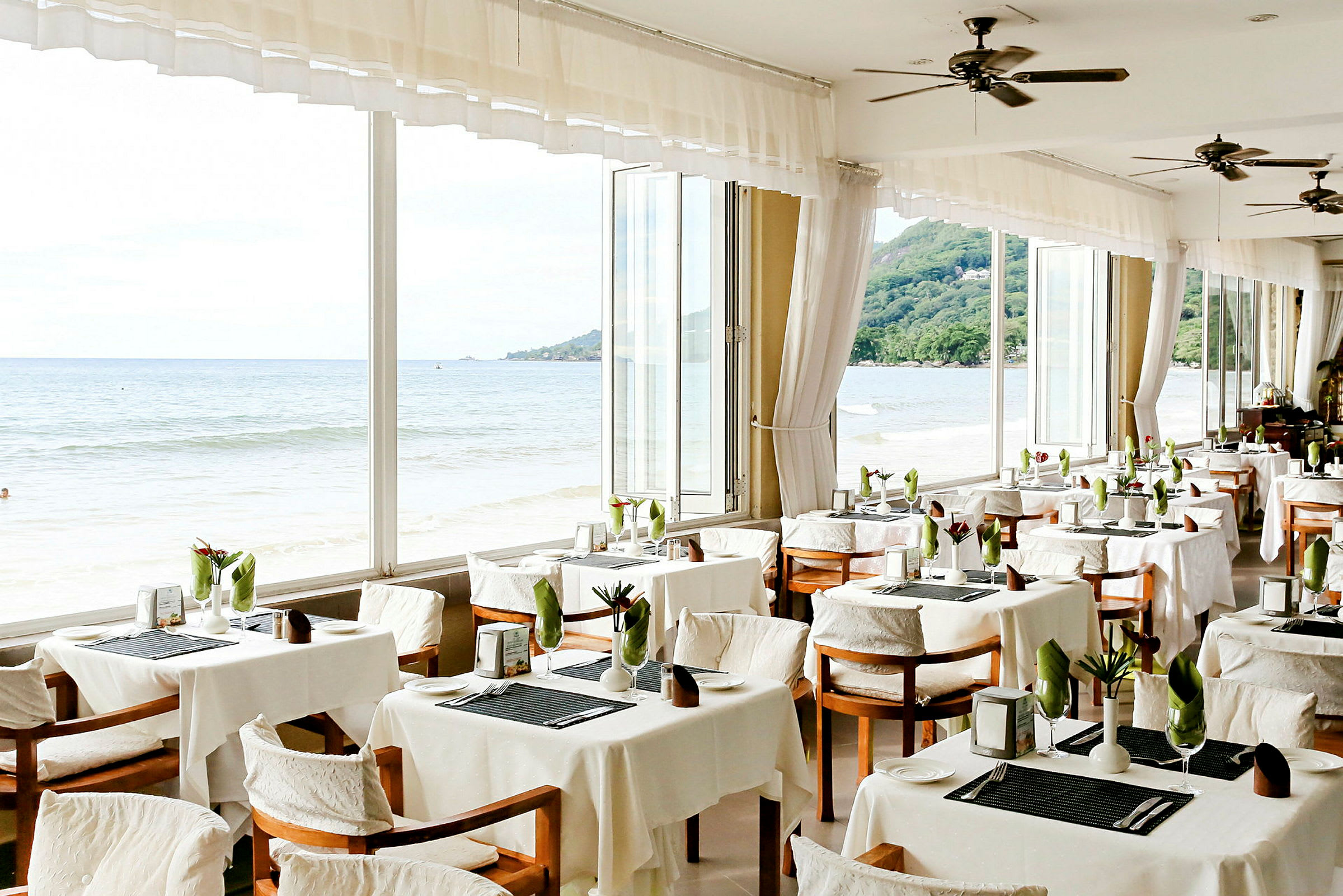 Restaurant med dekkede bord og utsikt over havet gjennom store vinduer. (AI-generert tekst)
