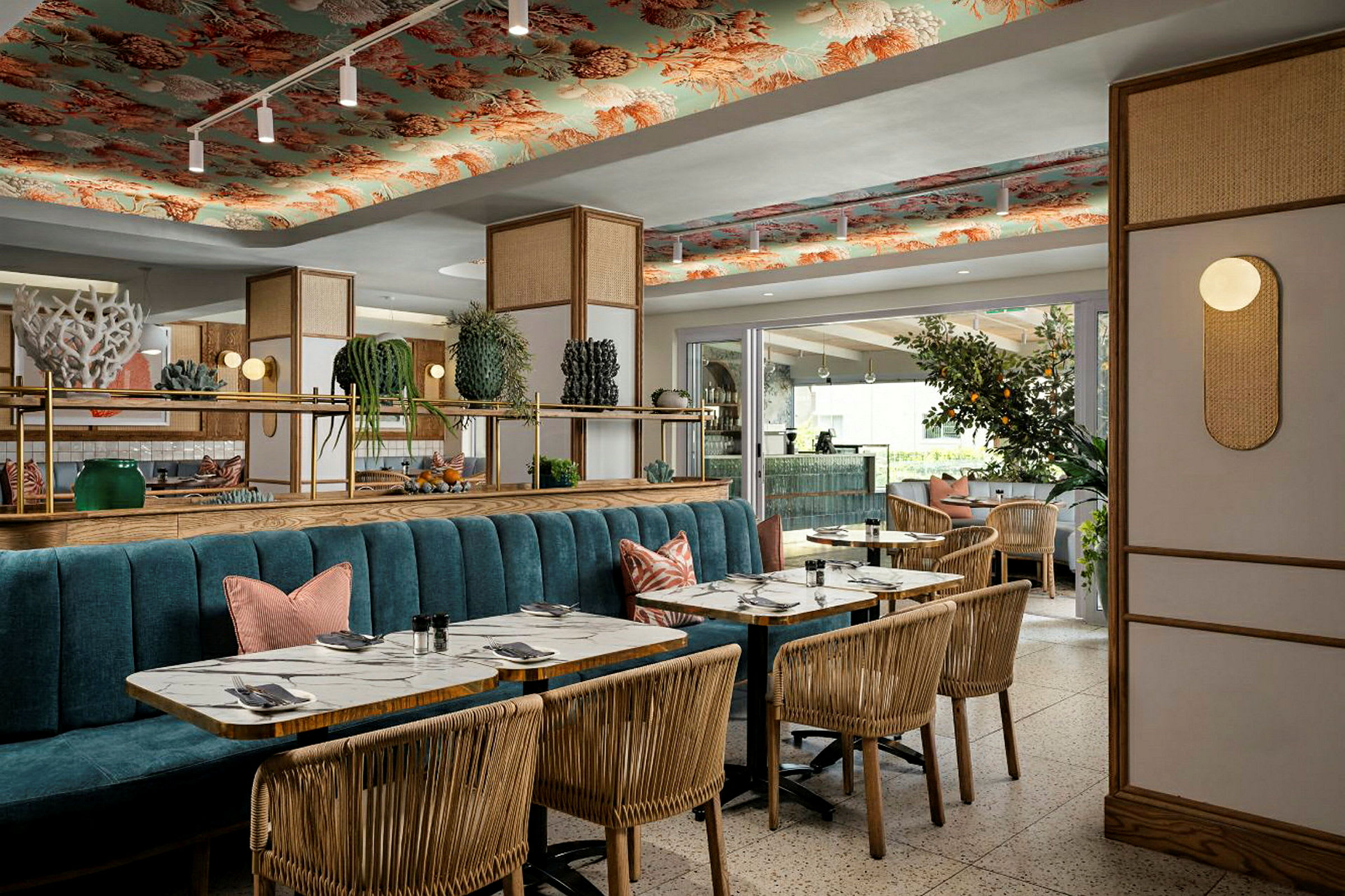 Et elegant restaurantinteriør med trestoler, marmorbord og en blå sofabenk. Taket er dekorert med mønstre, og interiøret fullføres med planter og belysning. (AI-generert tekst)