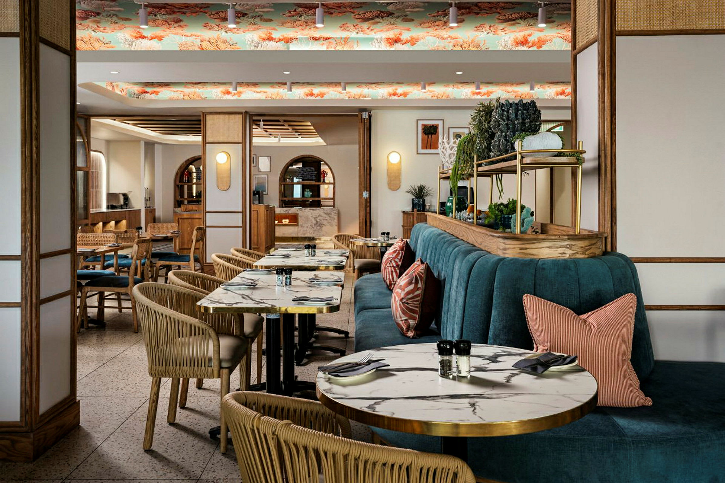 En restaurantinteriør med marmorerte bord, rottingstoler og en turkis sittebenk med puter. Taket har dekorativt mønster. (AI-generert tekst)
